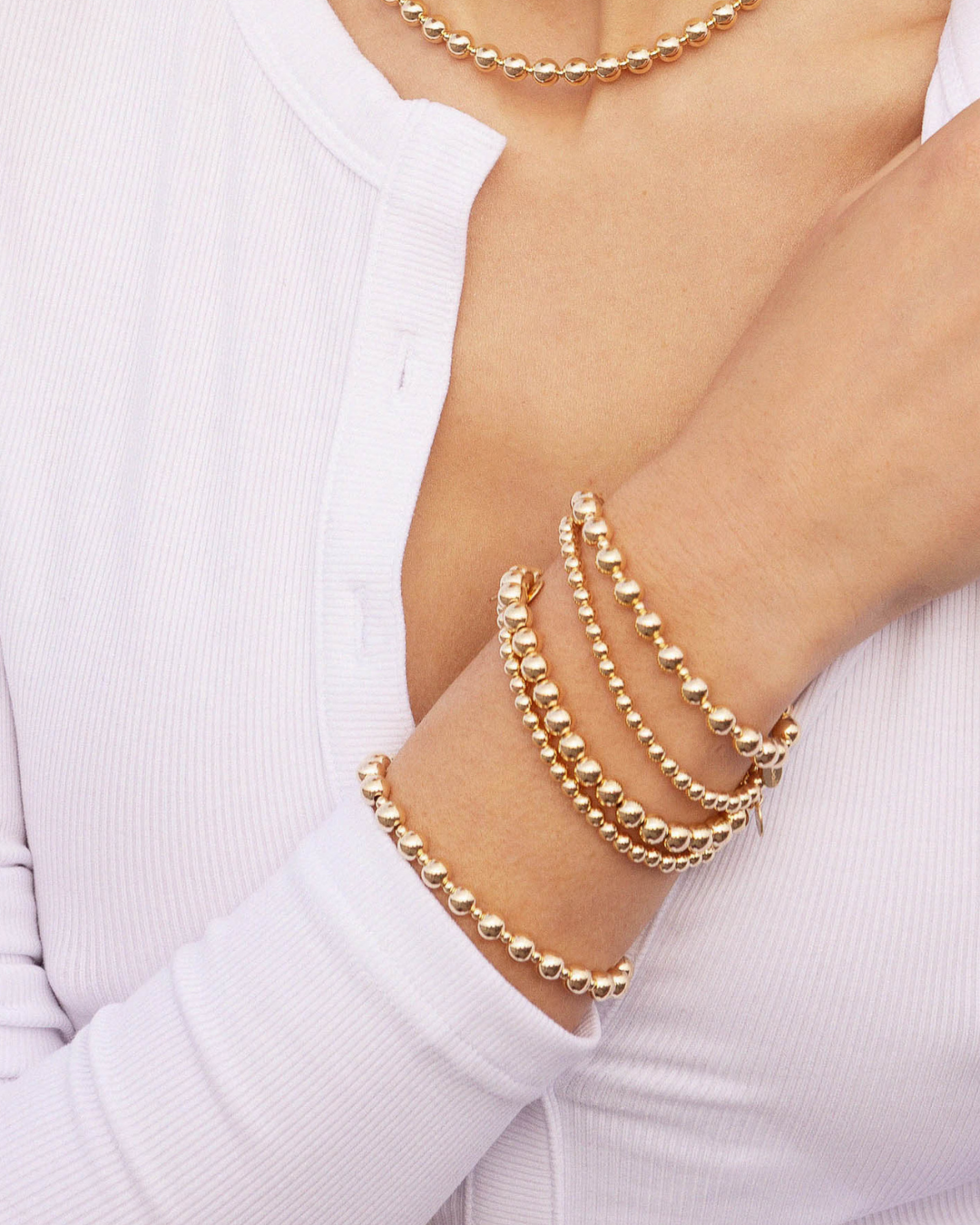 Gold beaded bracelets on a person's wrist with a white background