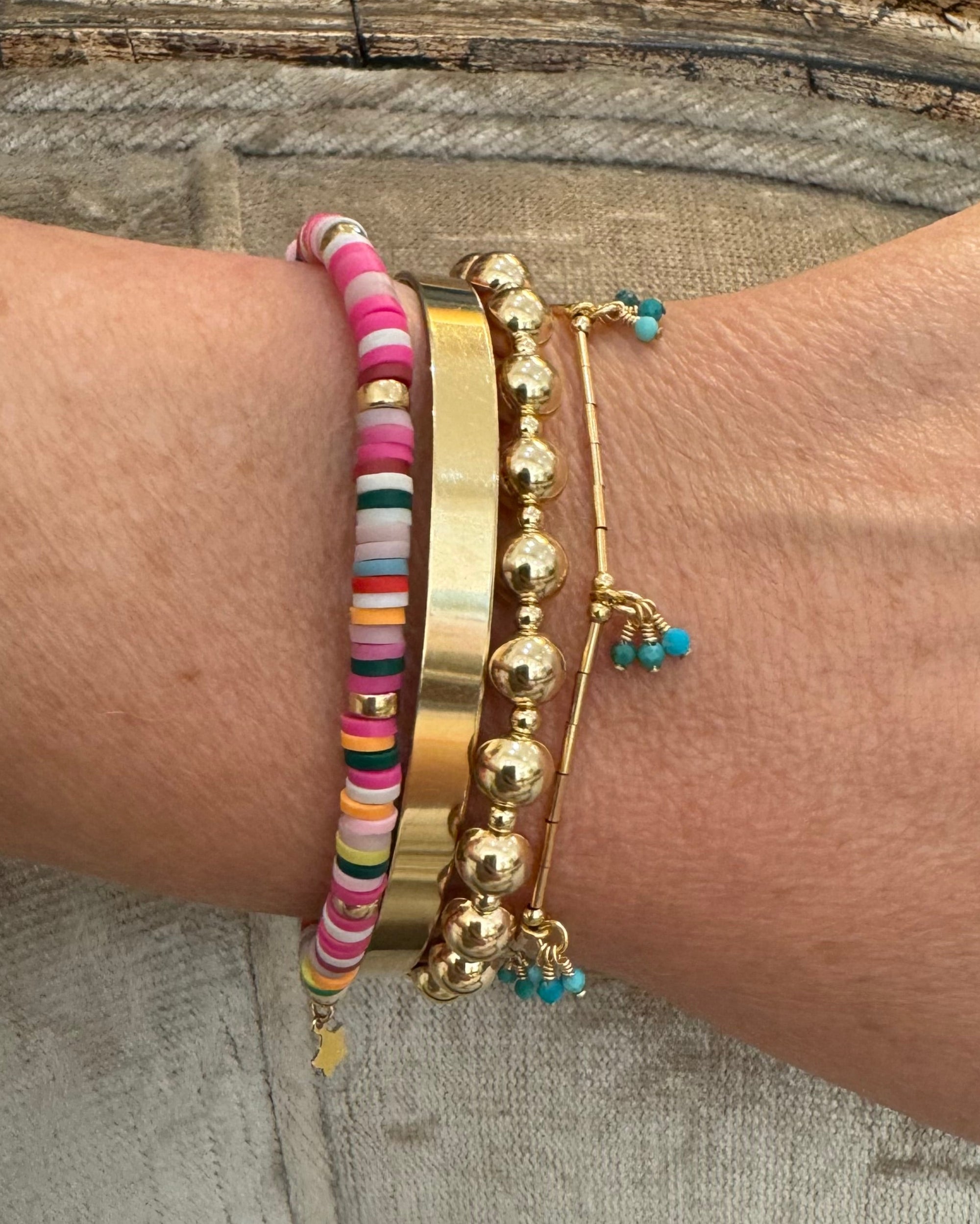 Wrist wearing a gold bead bracelet with a colorful beaded bracelets and a bracelete featuring turquoise gemstones on a textured surface