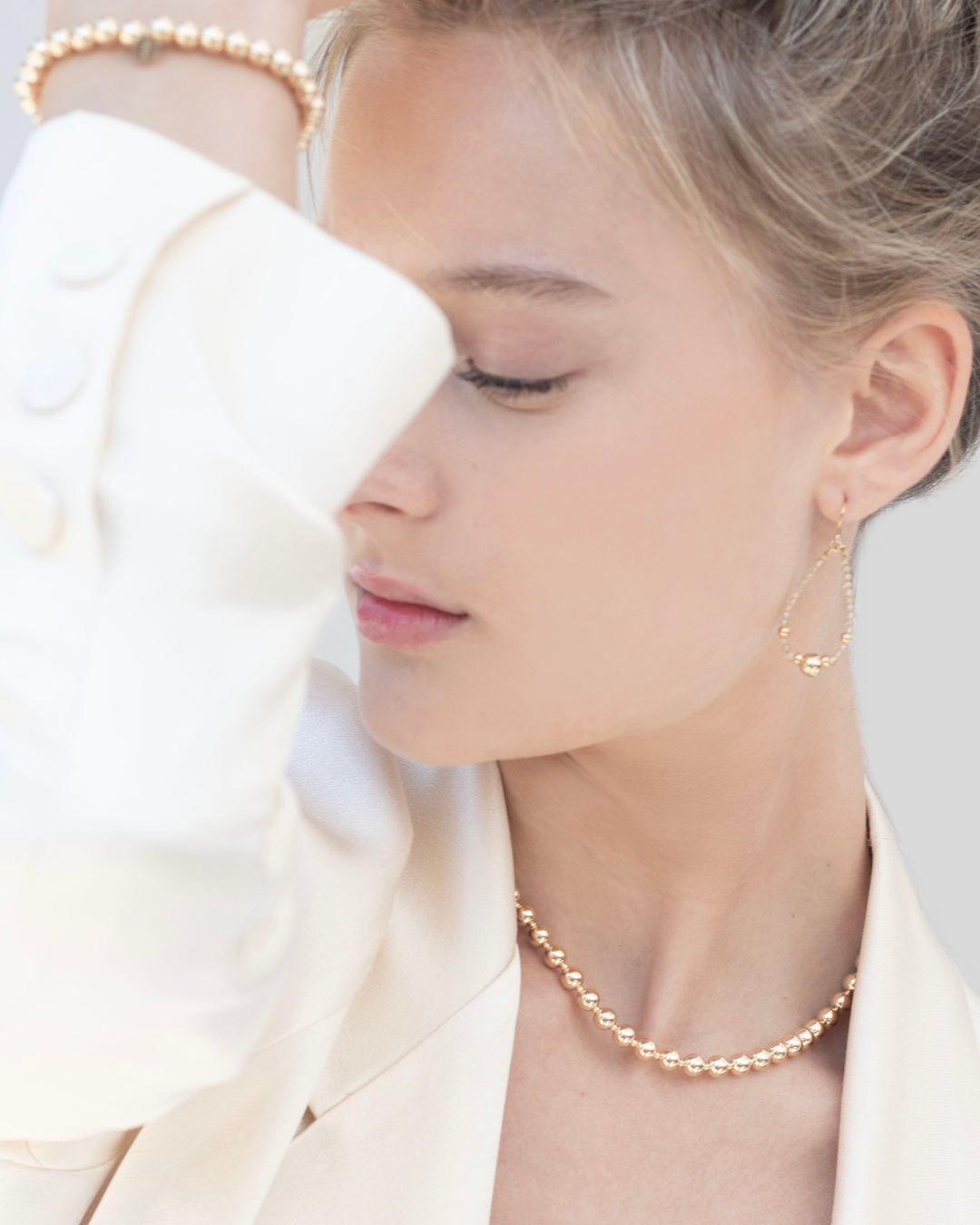 Close-up of a person wearing a gold bracelet, necklace and zircon gemstone earrings with a blurred background