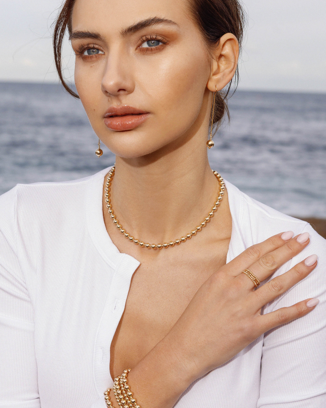 Woman wearing gold jewelry with a blurred ocean background