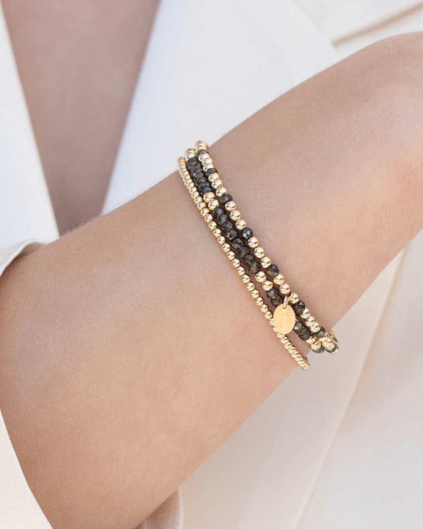 Close up of a wrist wearing gold and dark green zircon gemstone beaded bracelets.