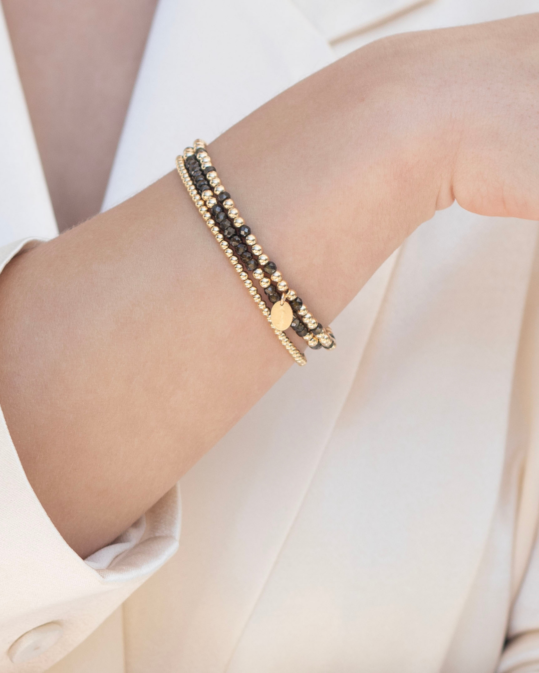 Close up of wrist wearing beaded gold and dark green zircon gemstone bracelets.