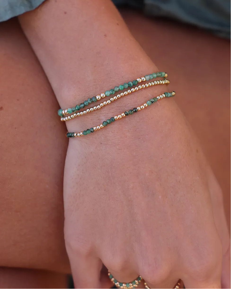 Model wearing bracelet with Emerald gems in shades of green, complemented by gold accent beads