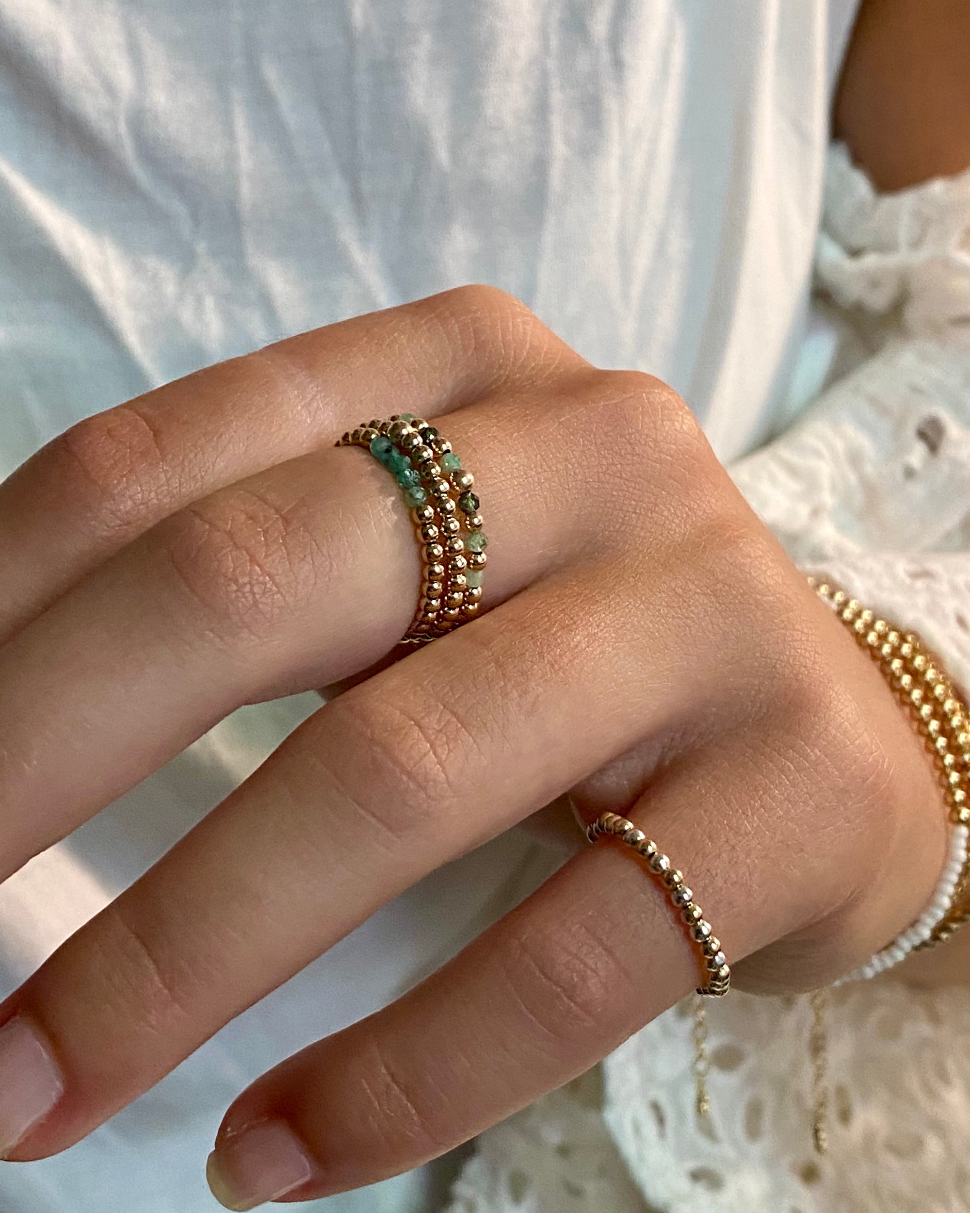 Close-up of a hand wearing multiple gold emerald rings on a light background