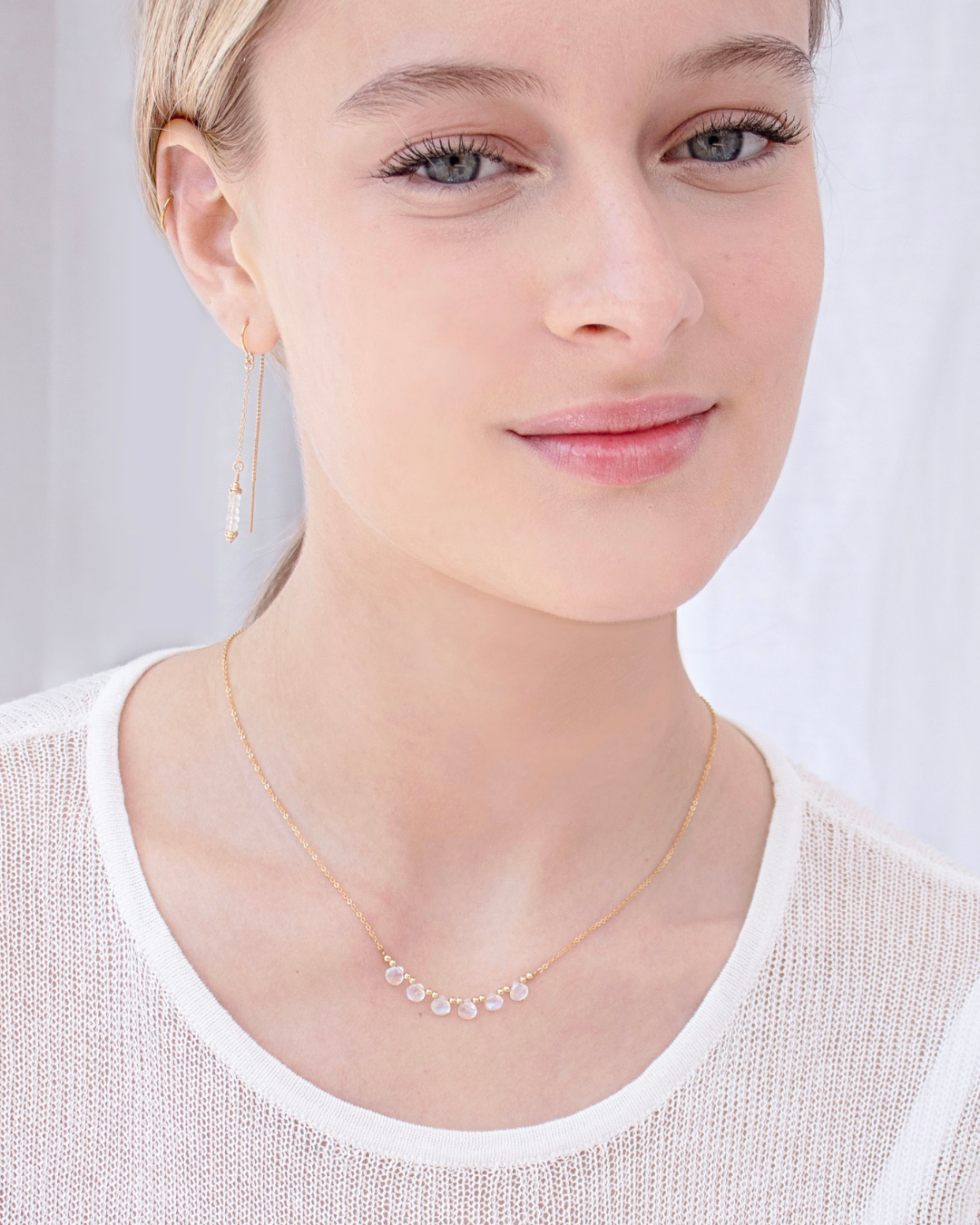 Woman wearing a delicate gold thread moonstone earring and necklace with a plain background