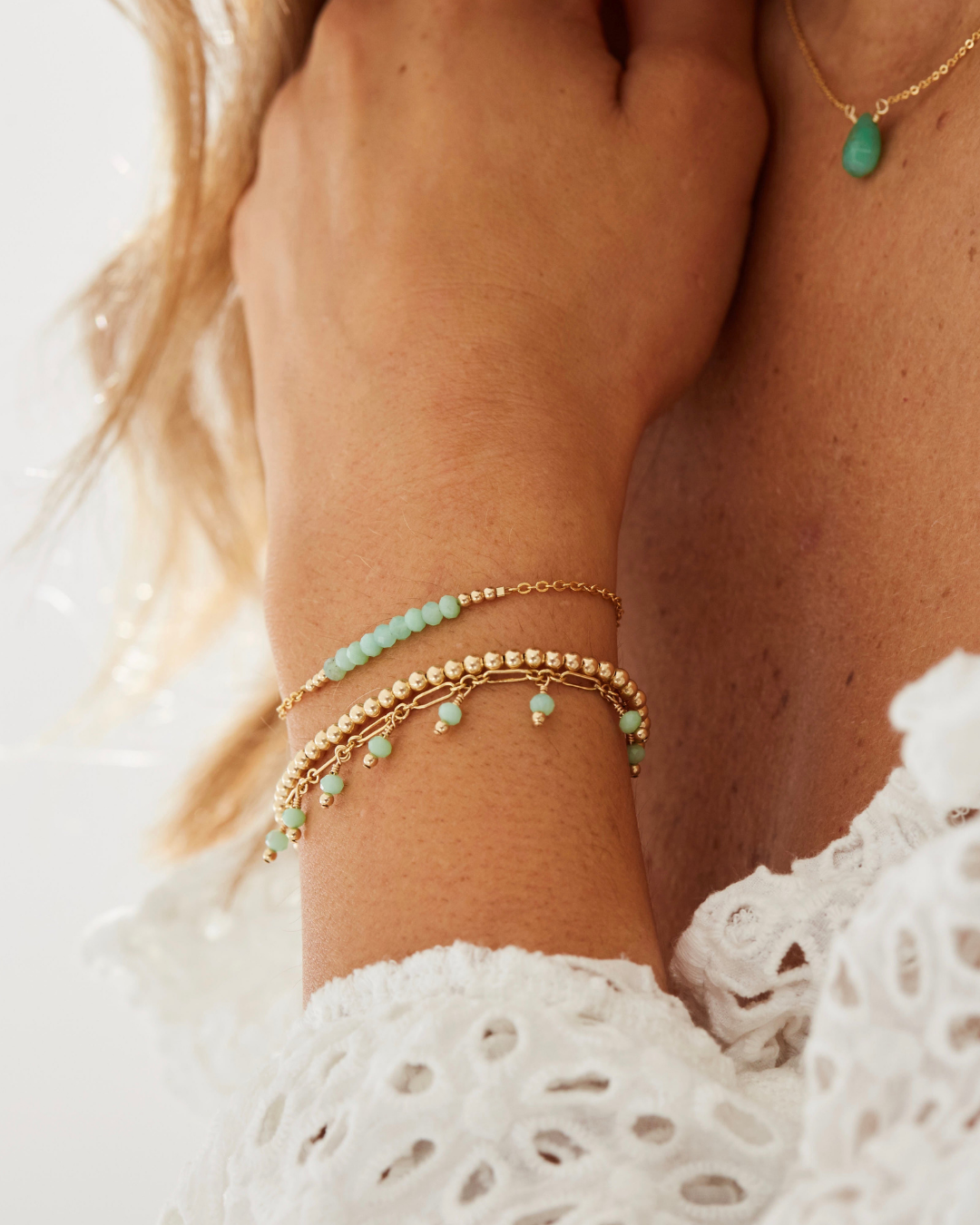 Close-up of a person's wrist wearing gold and chrysoprase beaded bracelets on a light background