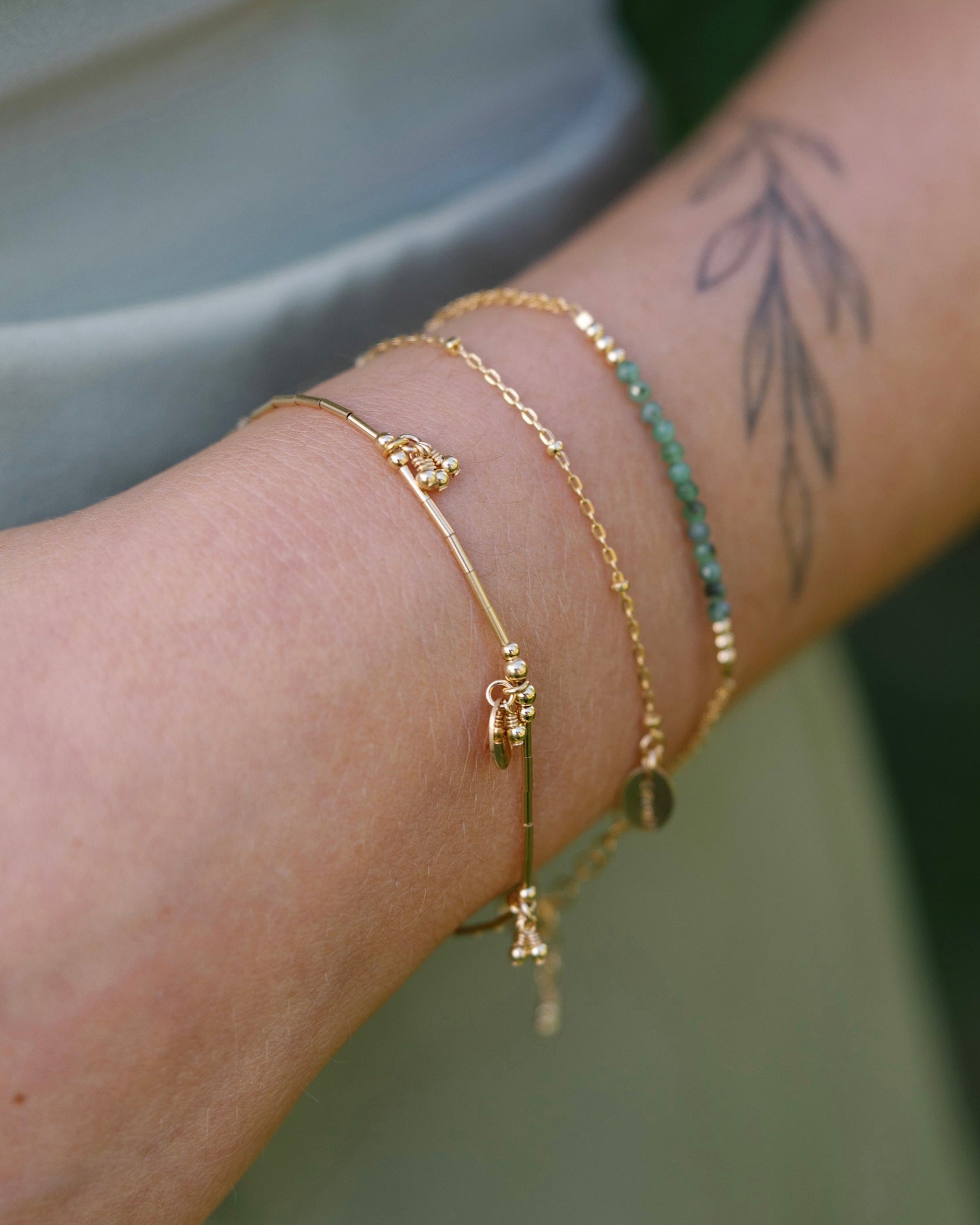 Close-up of a wrist wearing gold bracelets with and emerald bracelet with a blurred background