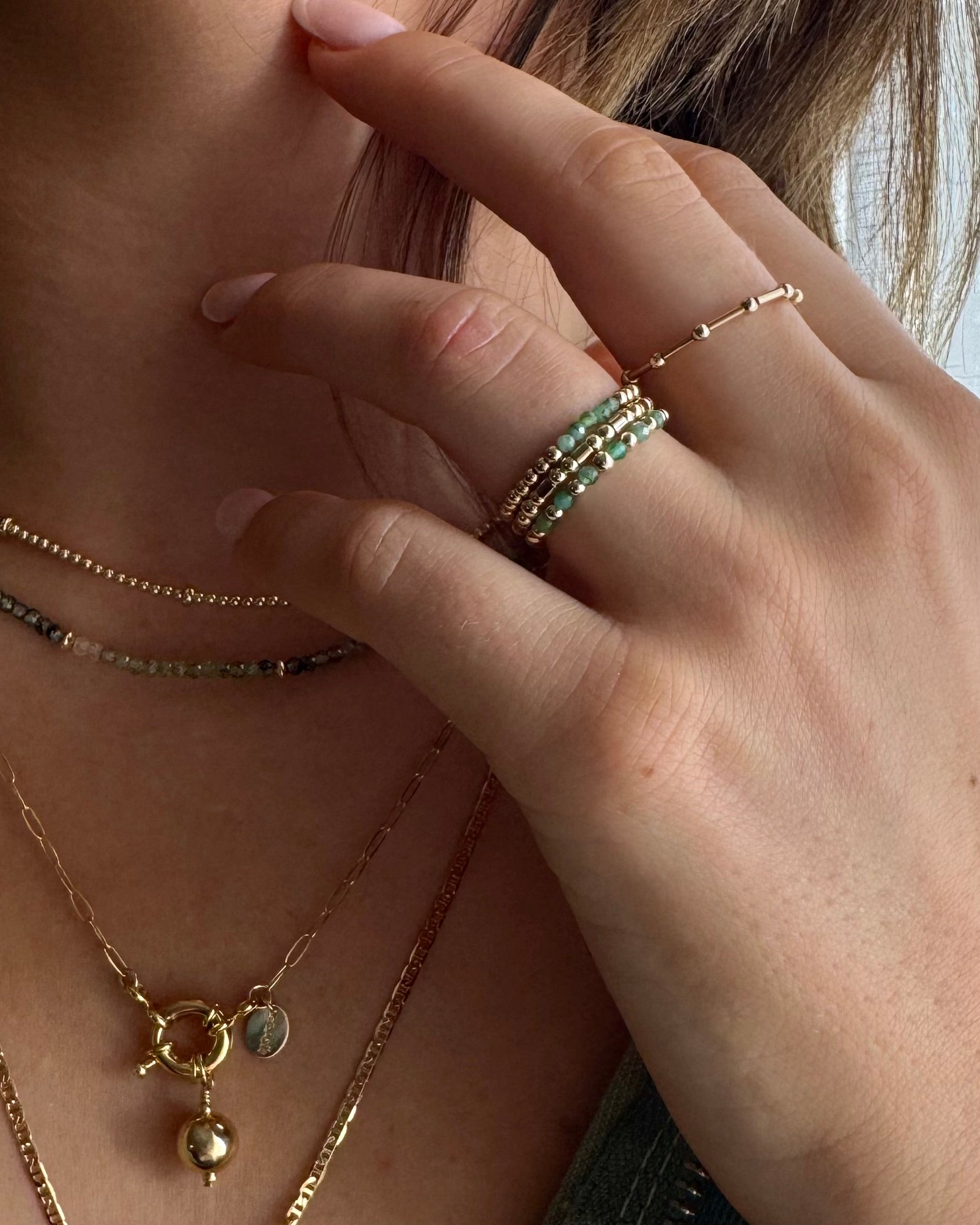 Close-up of a hand wearing emerald gold rings and gold necklaces with a blurred background