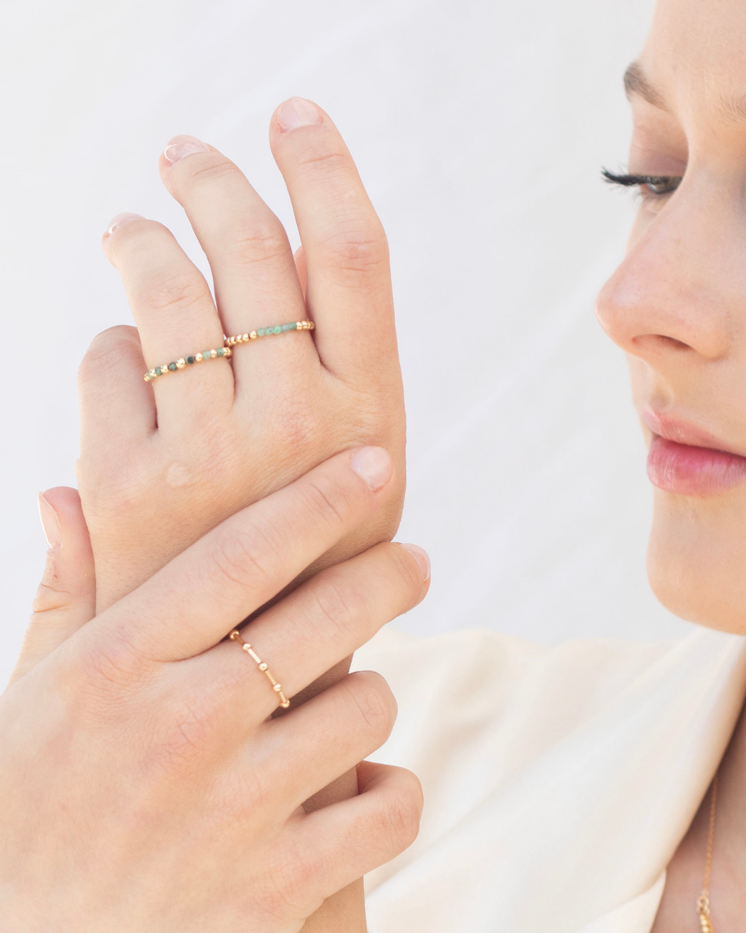 Close-up of a person wearing gold and emerald rings on a plain background