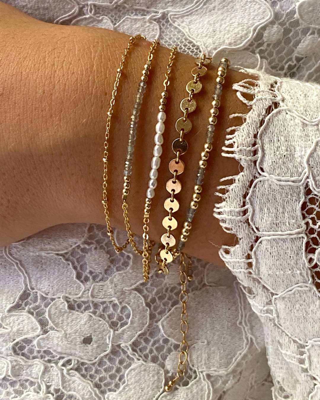 Gold and pearl beaded bracelets on a wrist with lace fabric background