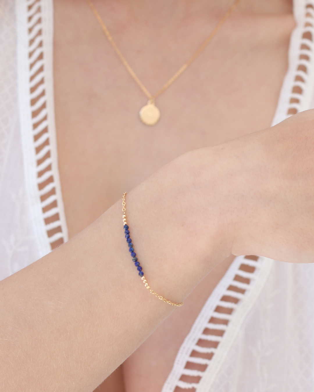 Gold bracelet with lapis lazuli gemstones on a woman wearing a white lace top.