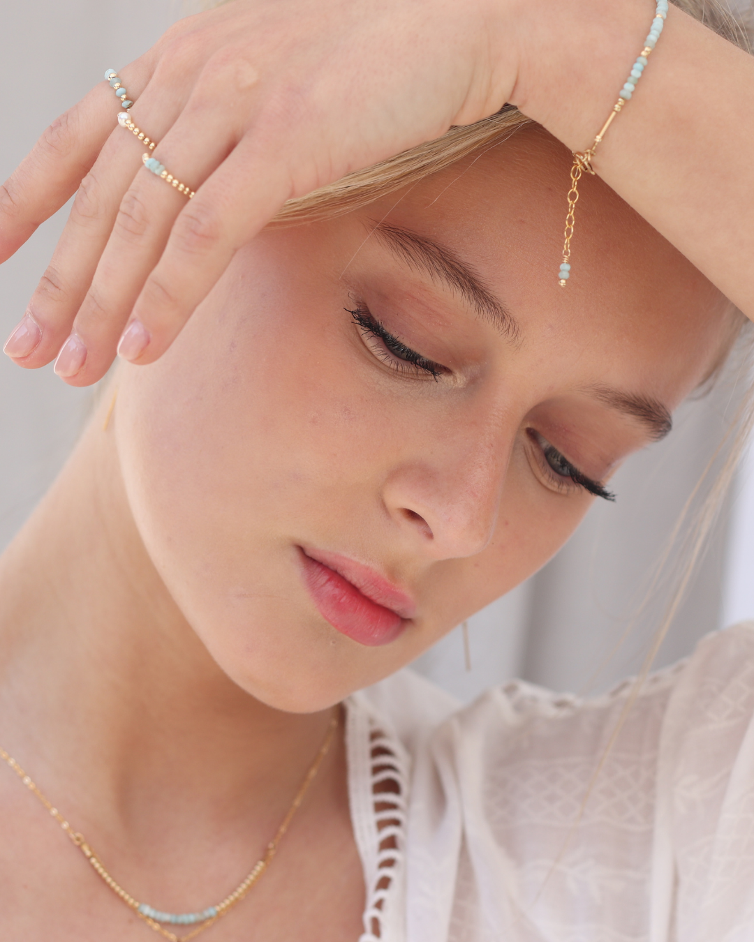 Close-up of a woman wearing gold and larimar rings, bracelet and necklace on a neutral background