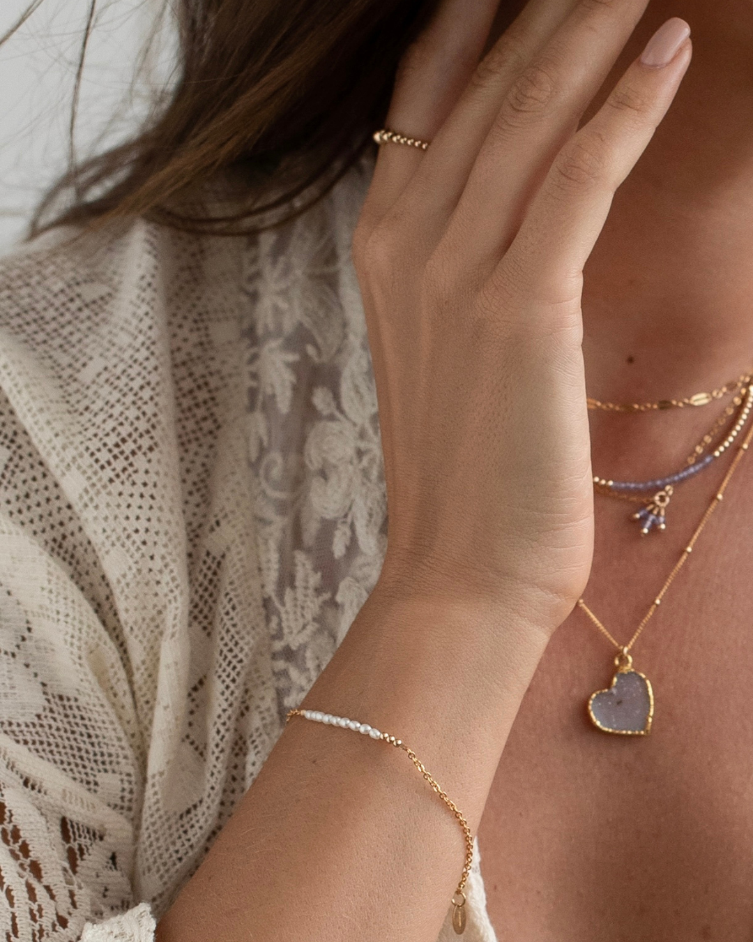 Close-up of a hand wearing multiple gold necklaces with heart pendants.