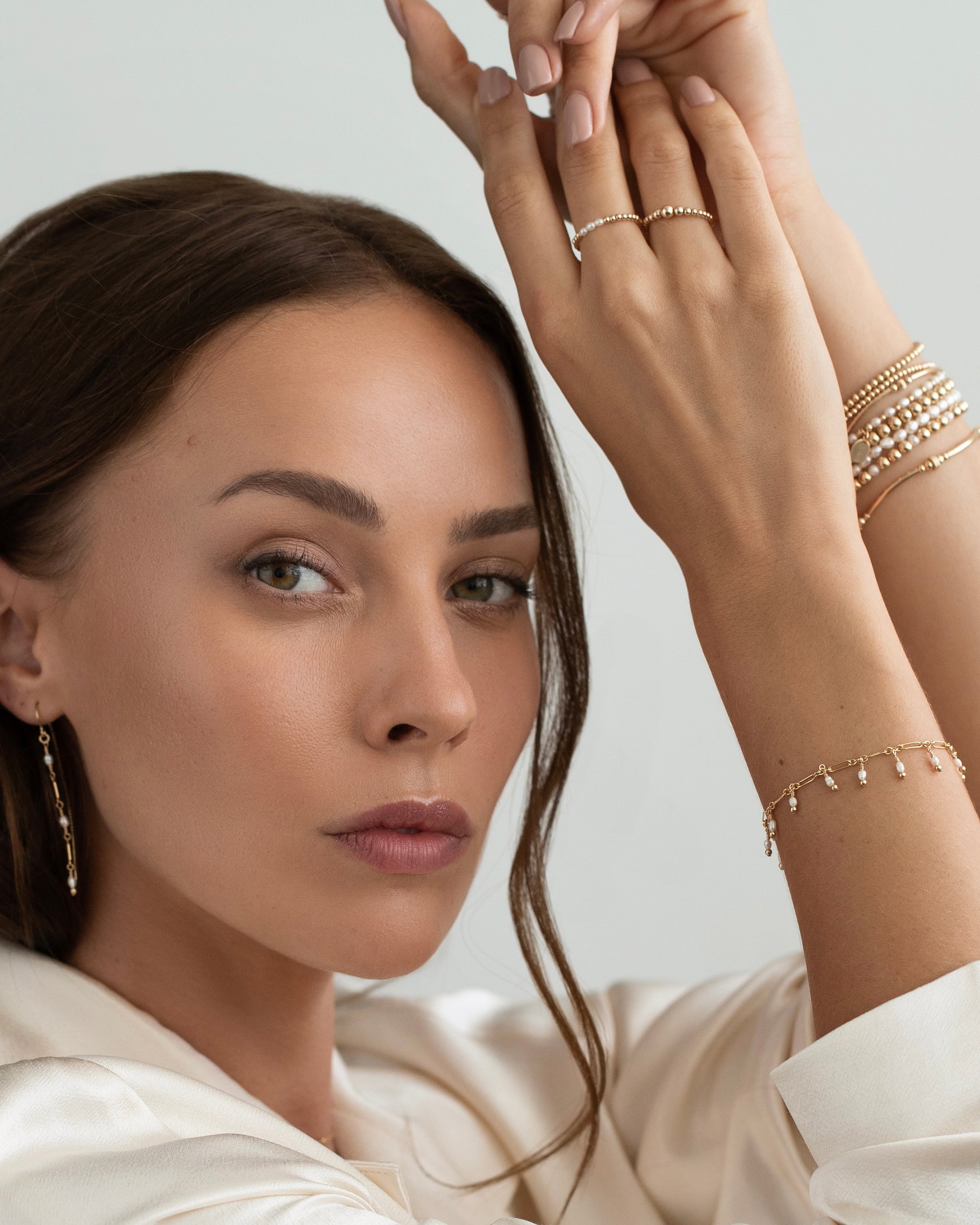 Woman wearing multiple gold pearl jewellery pieces including rings, bracelets and earrings.