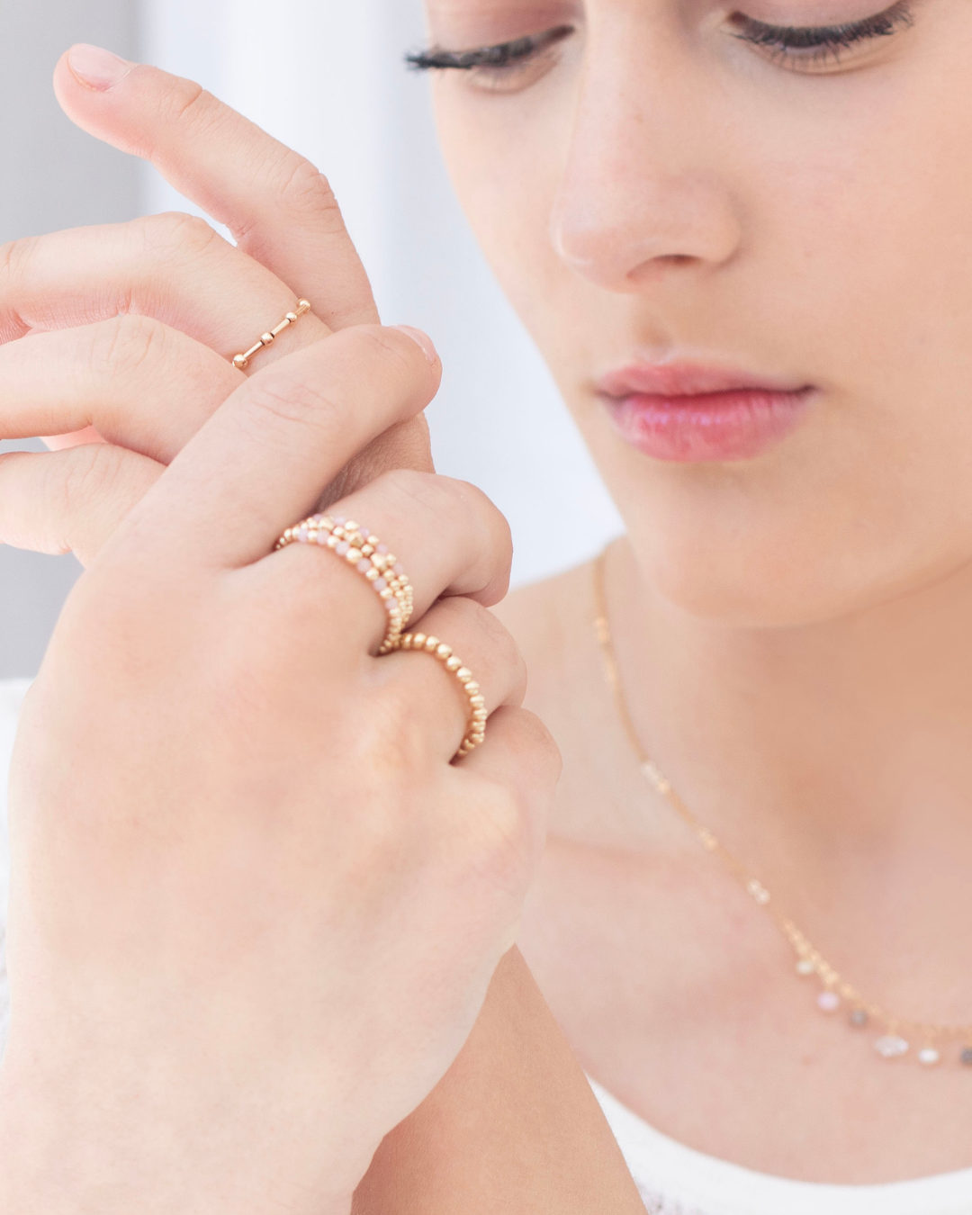 Close-up of a model wearing gold rings with pink peruvian opal gemstones on a plain background