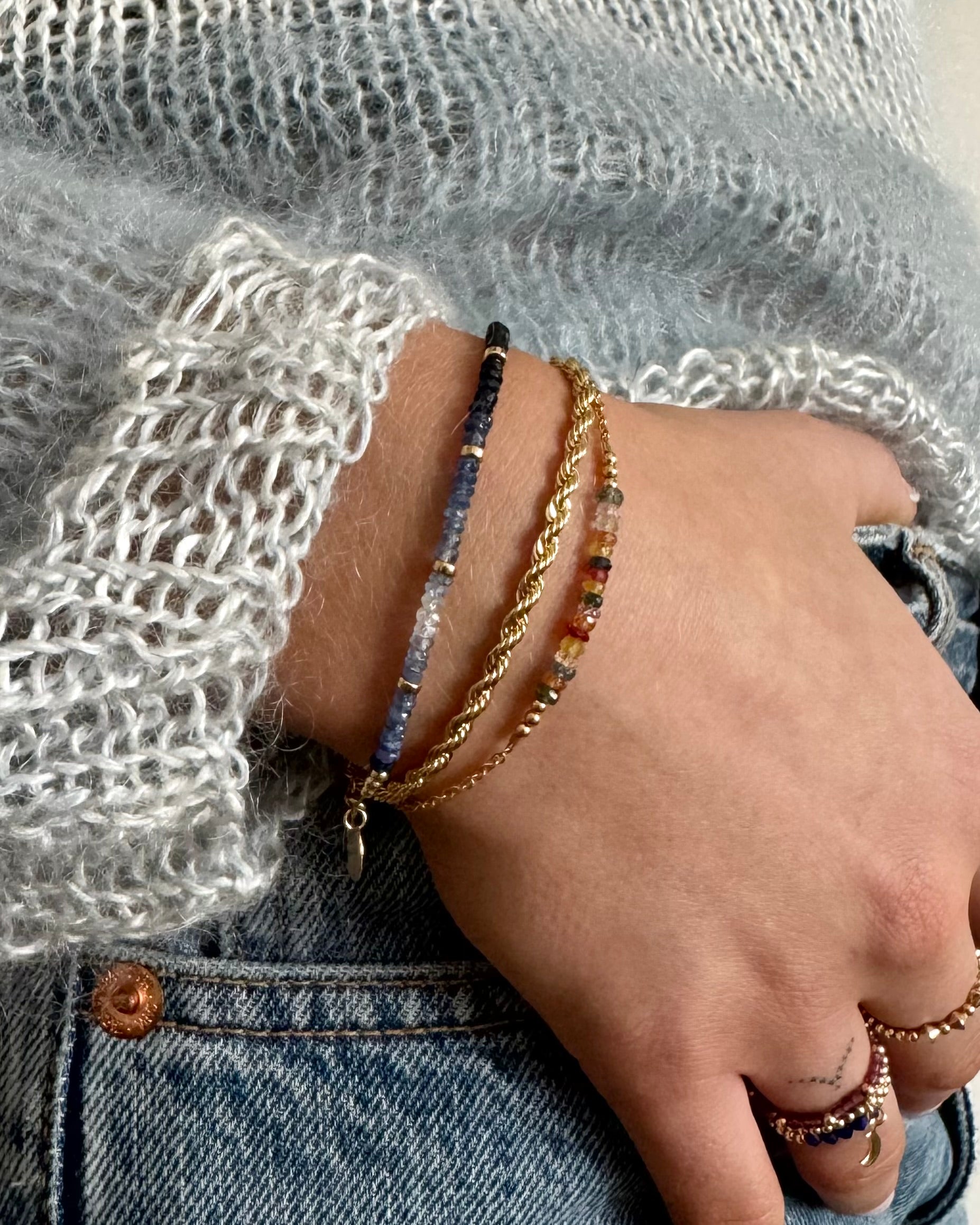 Hand wearing multiple bracelets and rings with a textured background of a jumper and jeans