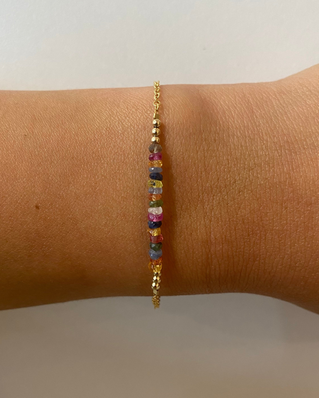 Gold chain bracelet with  multi colour beads on a close up of a wrist.