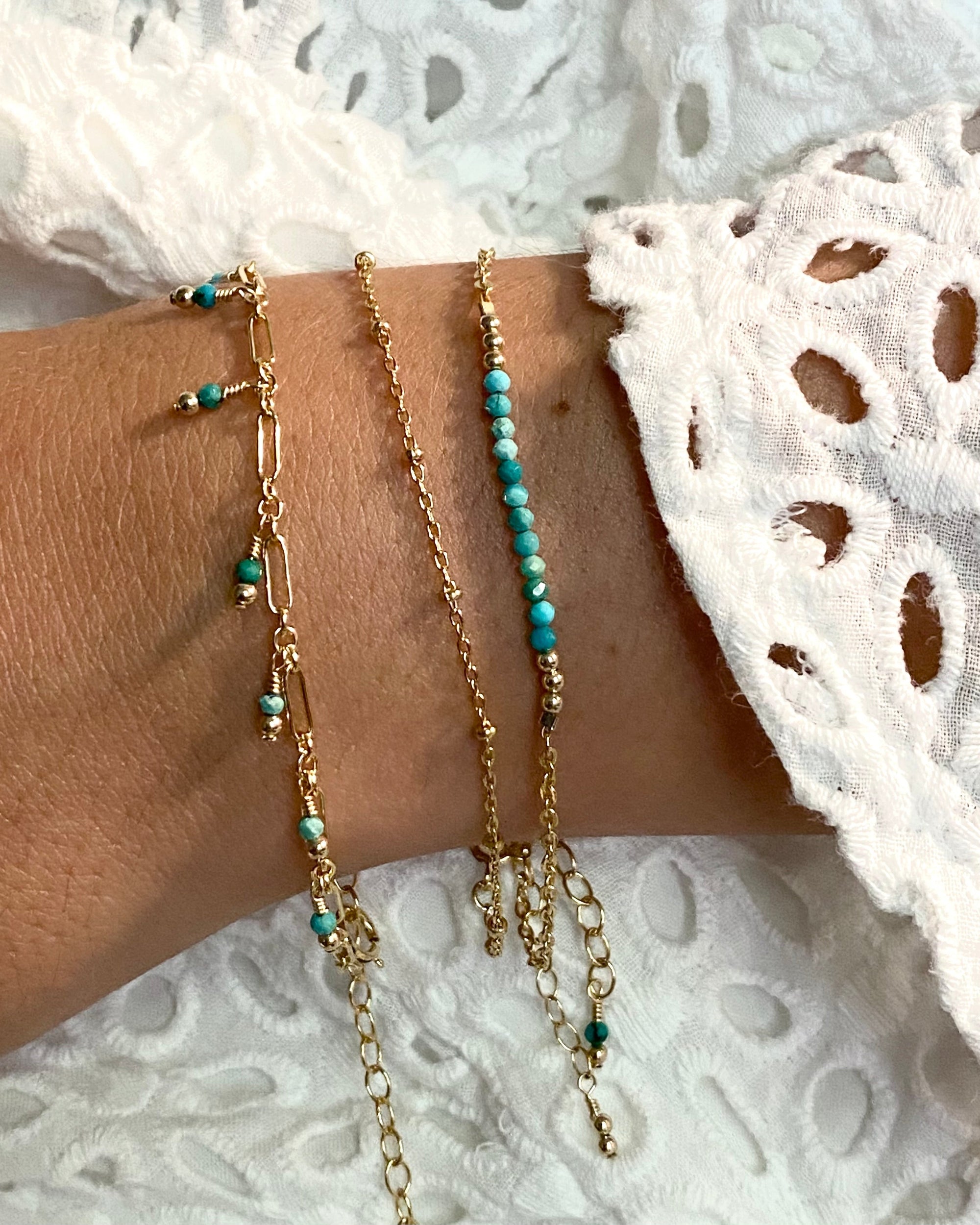 Gold and turquoise gemstone bracelets on a wrist with a white lace background