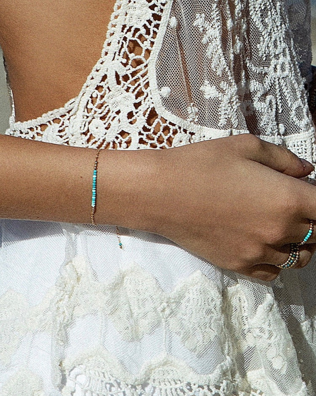 Close-up of a hand wearing multiple bracelets with a white lace garment in the background