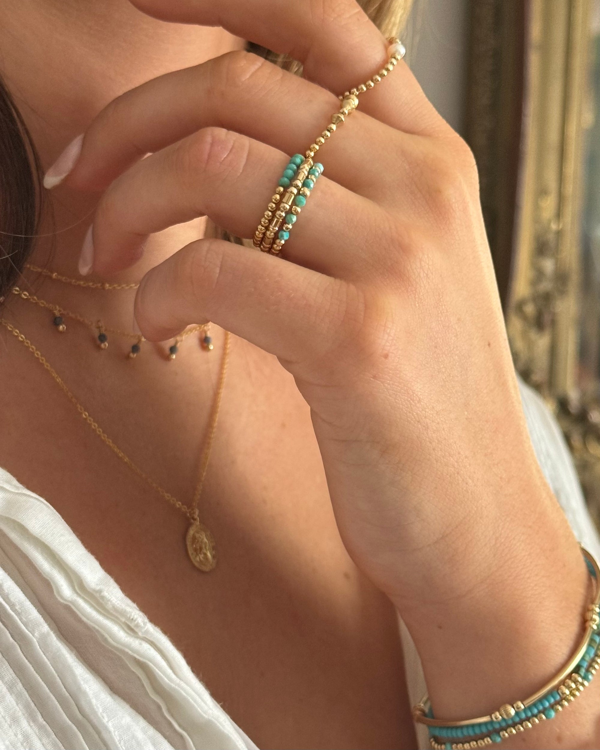 Close-up of a woman's hand wearing multiple gold and turquoise rings and bracelets.