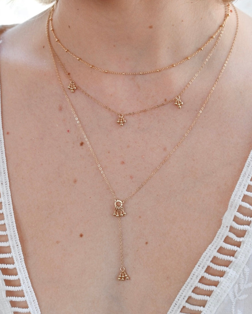 Close-up of a person wearing a delicate gold necklace with small pendants against a blurred background.