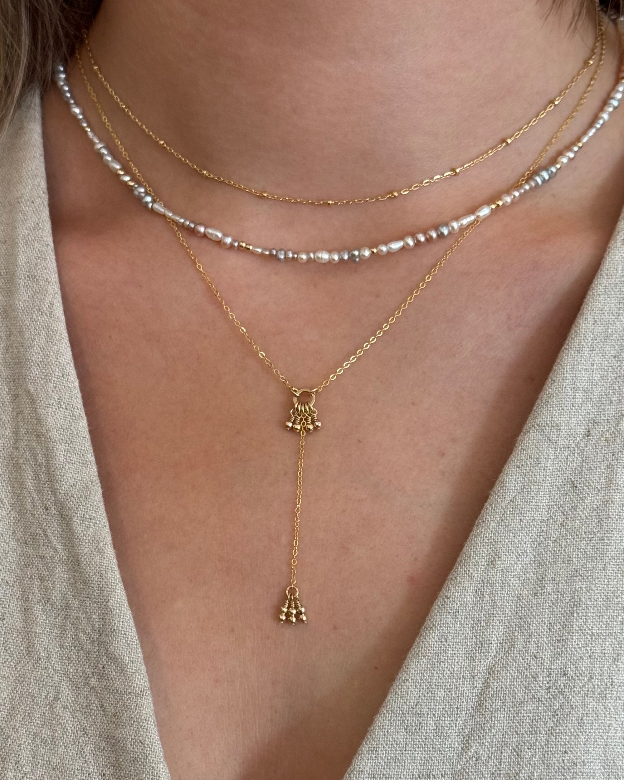 Close-up of a person wearing layered necklaces with a focus on a gold necklace with a bell pendant.