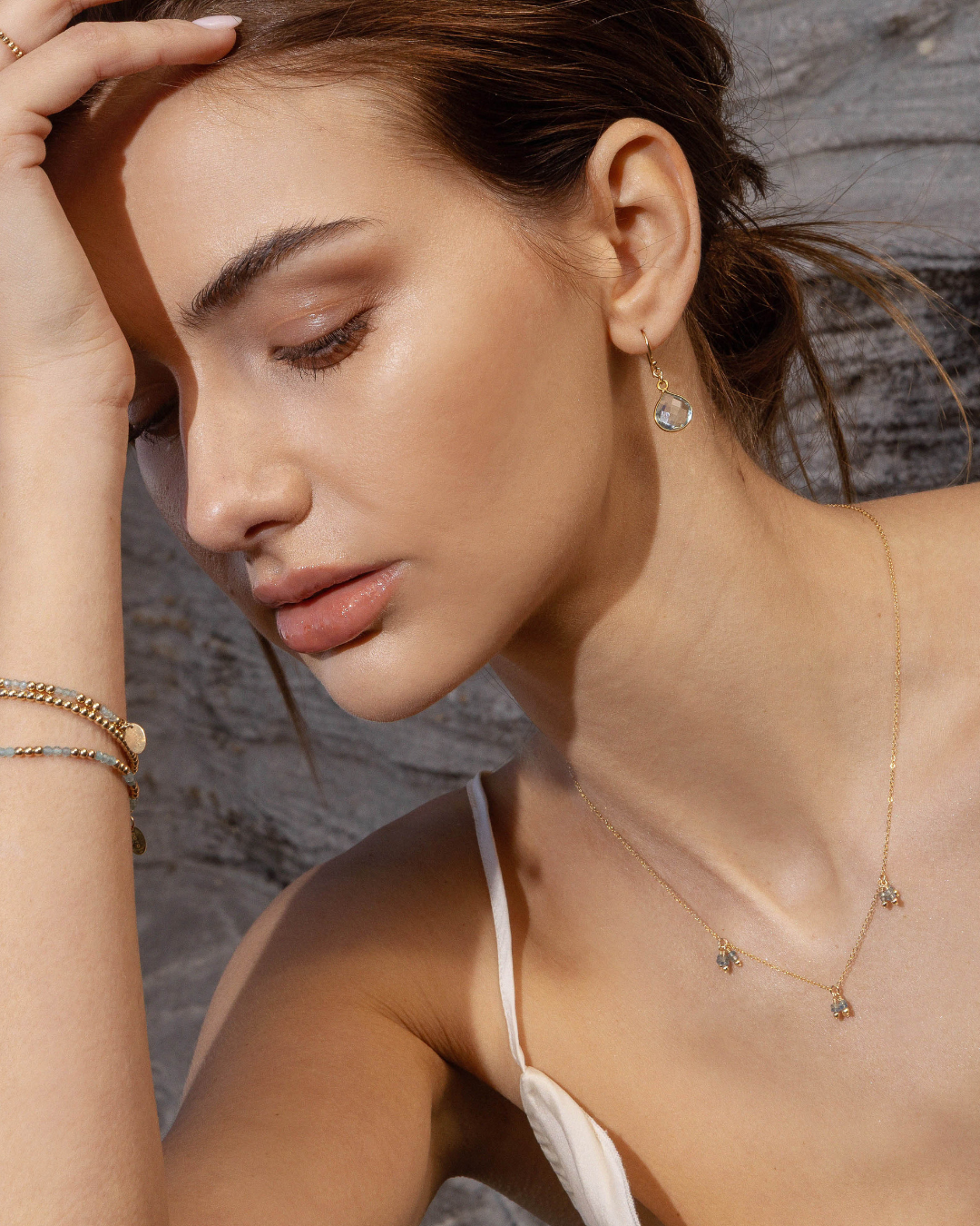Close-up of a woman wearing gold jewelry against a stone wall background