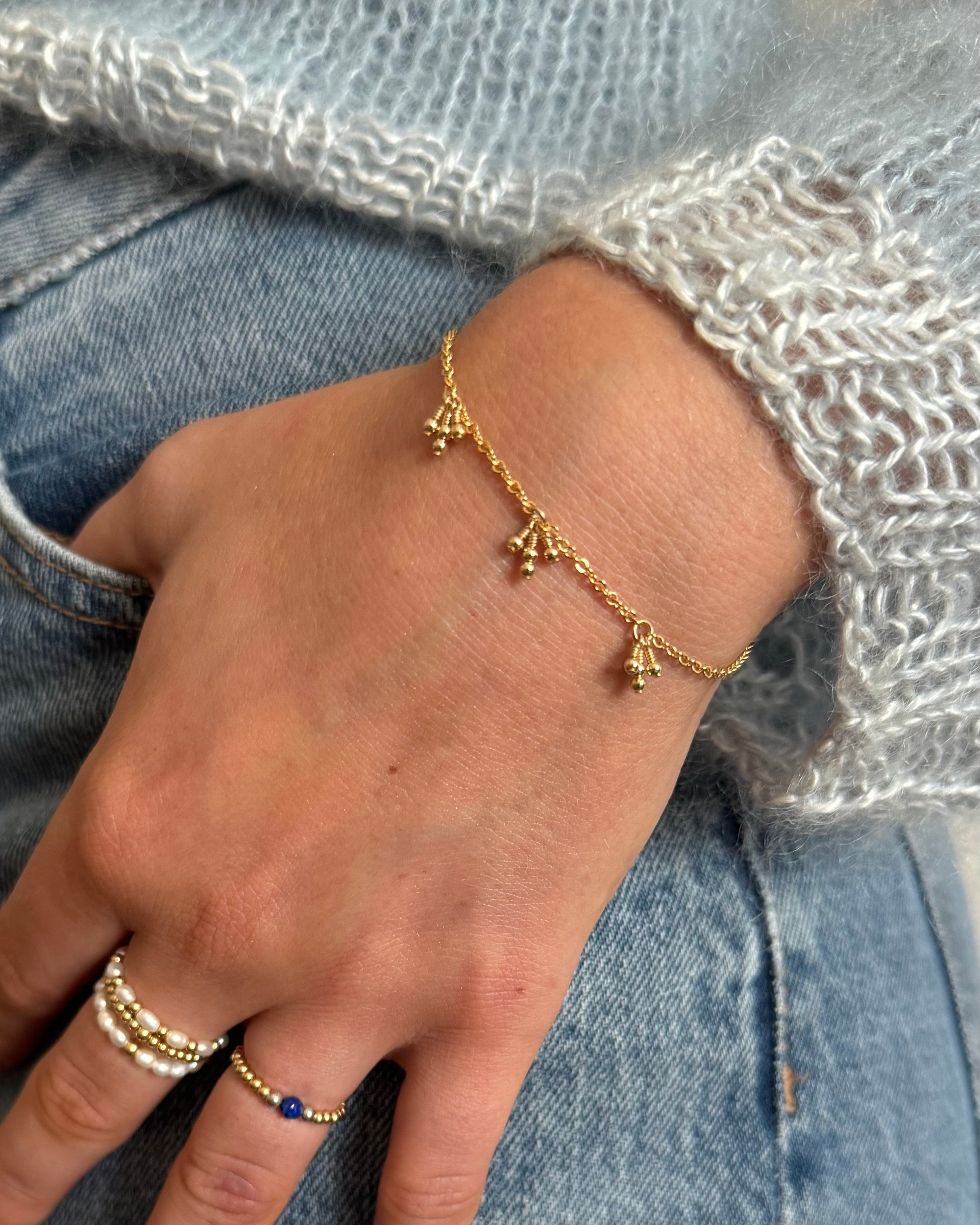 Gold bracelet on a wrist with denim jeans and jumper in background