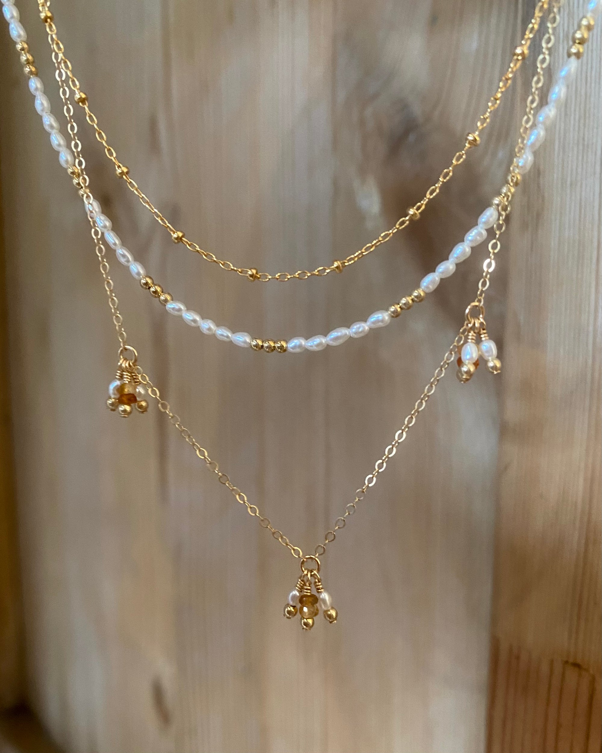 Three necklaces, gold, citrine and pearl suspended in front of a wooden door