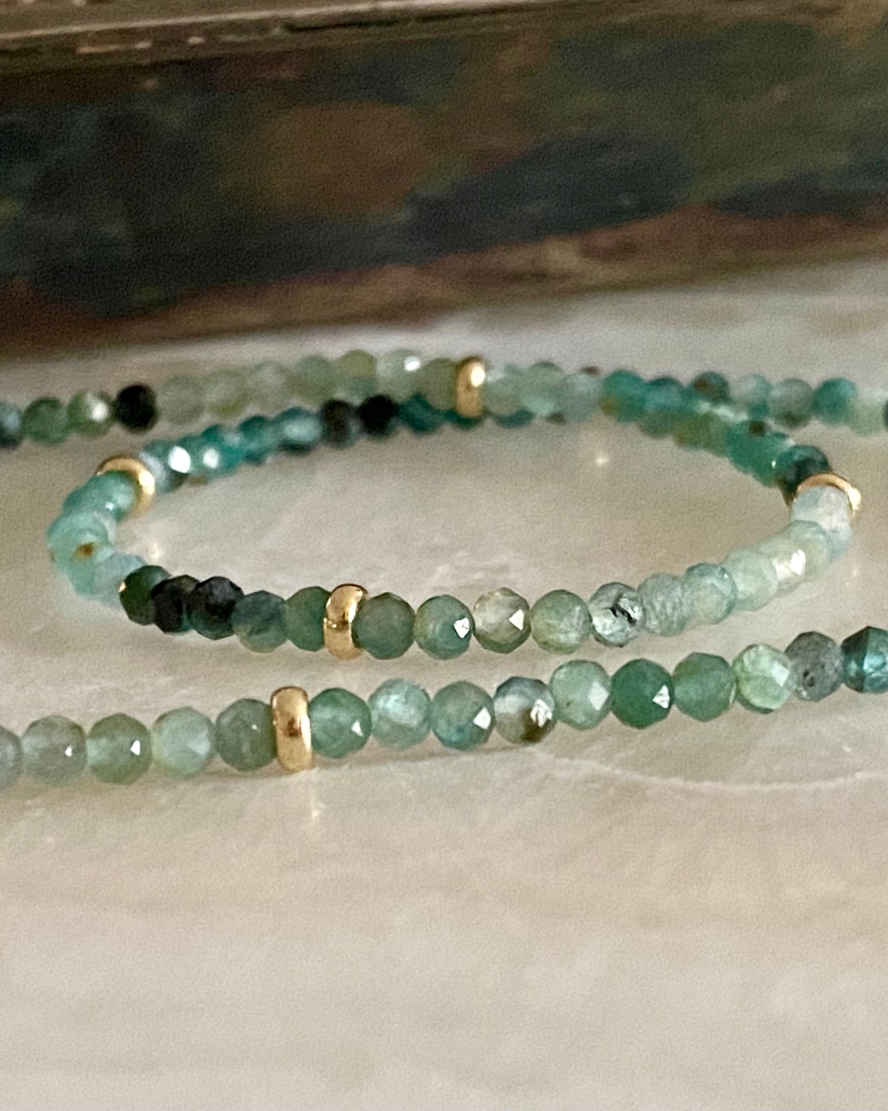 Gold beaded grandidierite gemstone necklace on a marble background