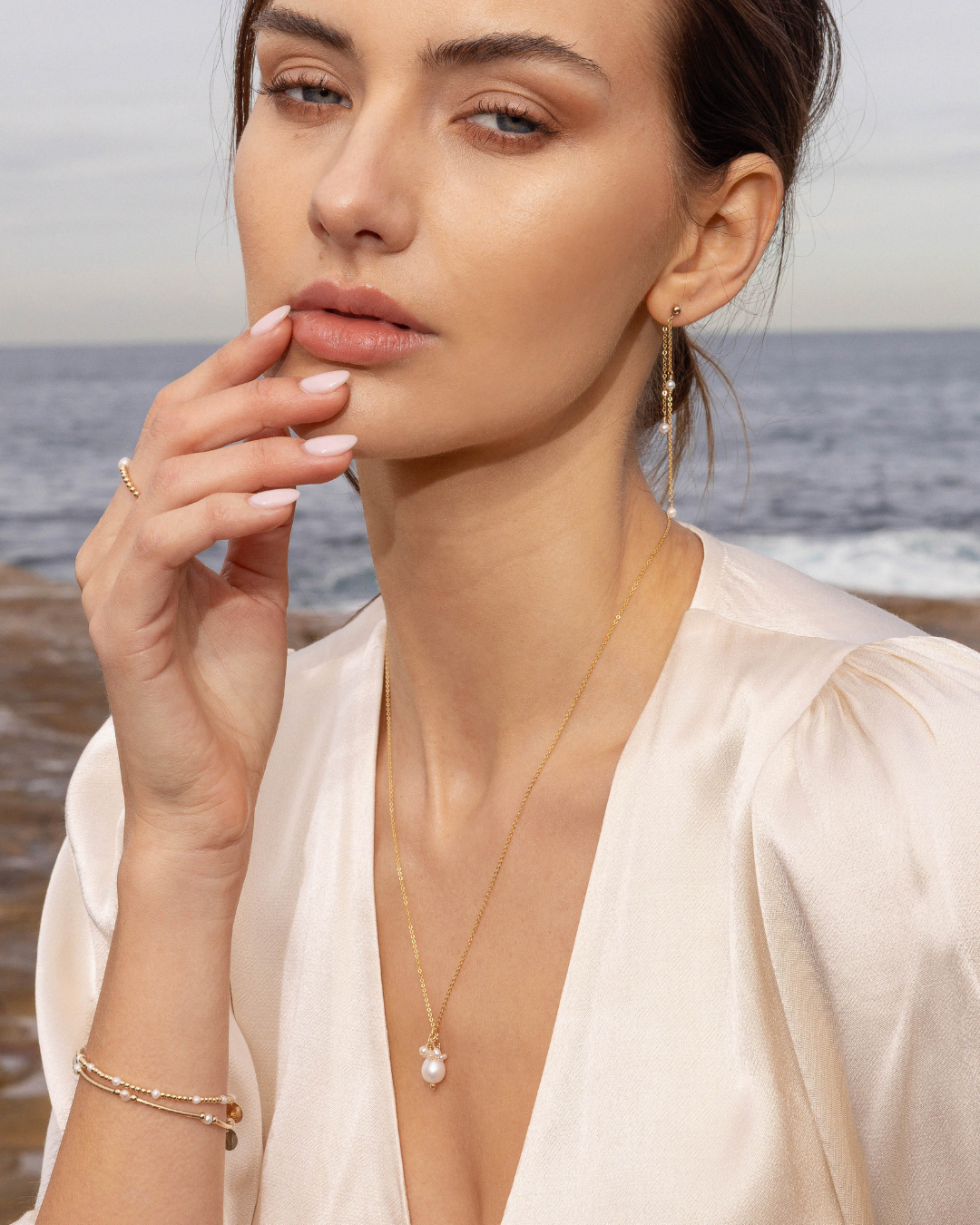 Woman wearing gold jewelry with a necklace and earrings by the ocean.