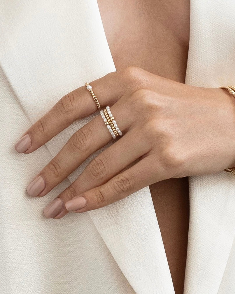 Hand wearing multiple gold pearl rings on a white fabric background