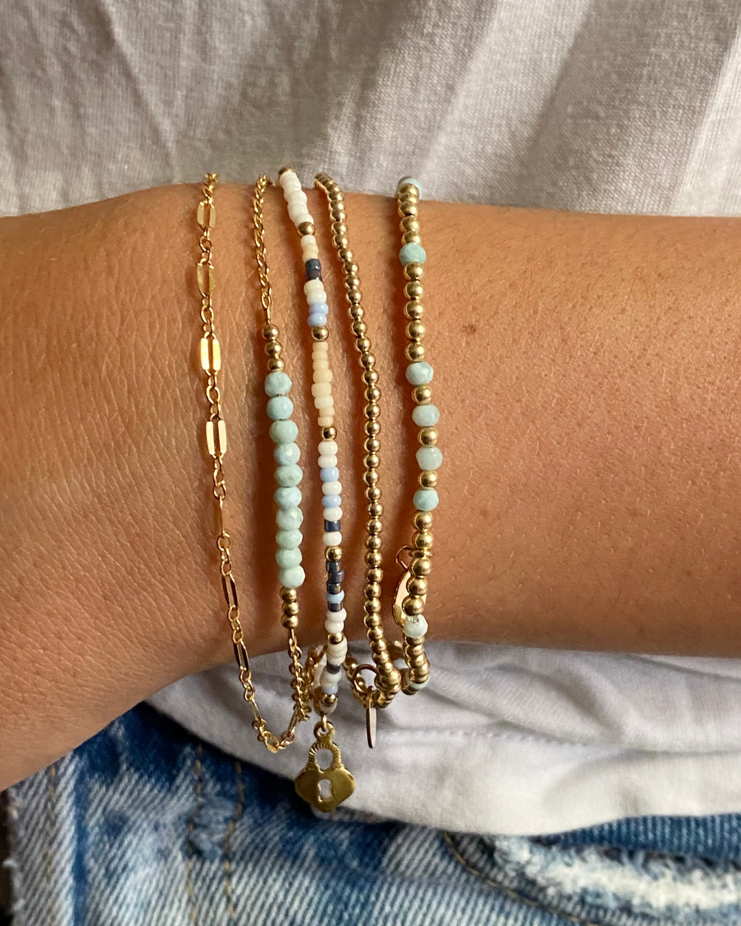 Close-up of a wrist wearing multiple beaded and gold bracelets on a neutral background.
