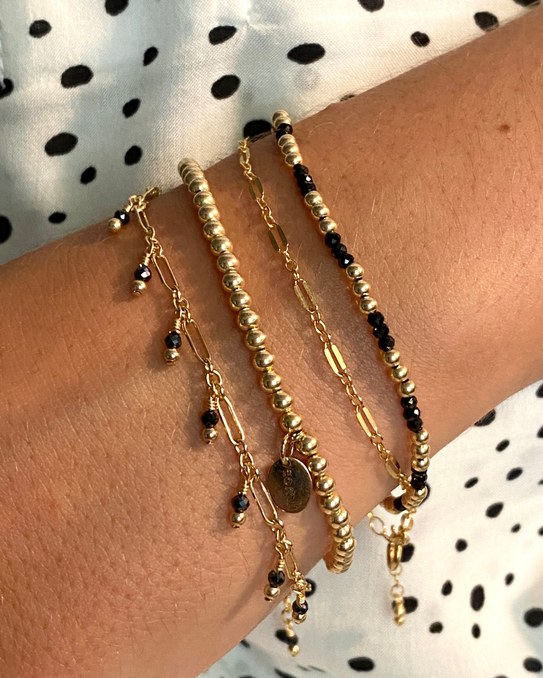 Gold and black beaded bracelets on a wrist with a polka dot background