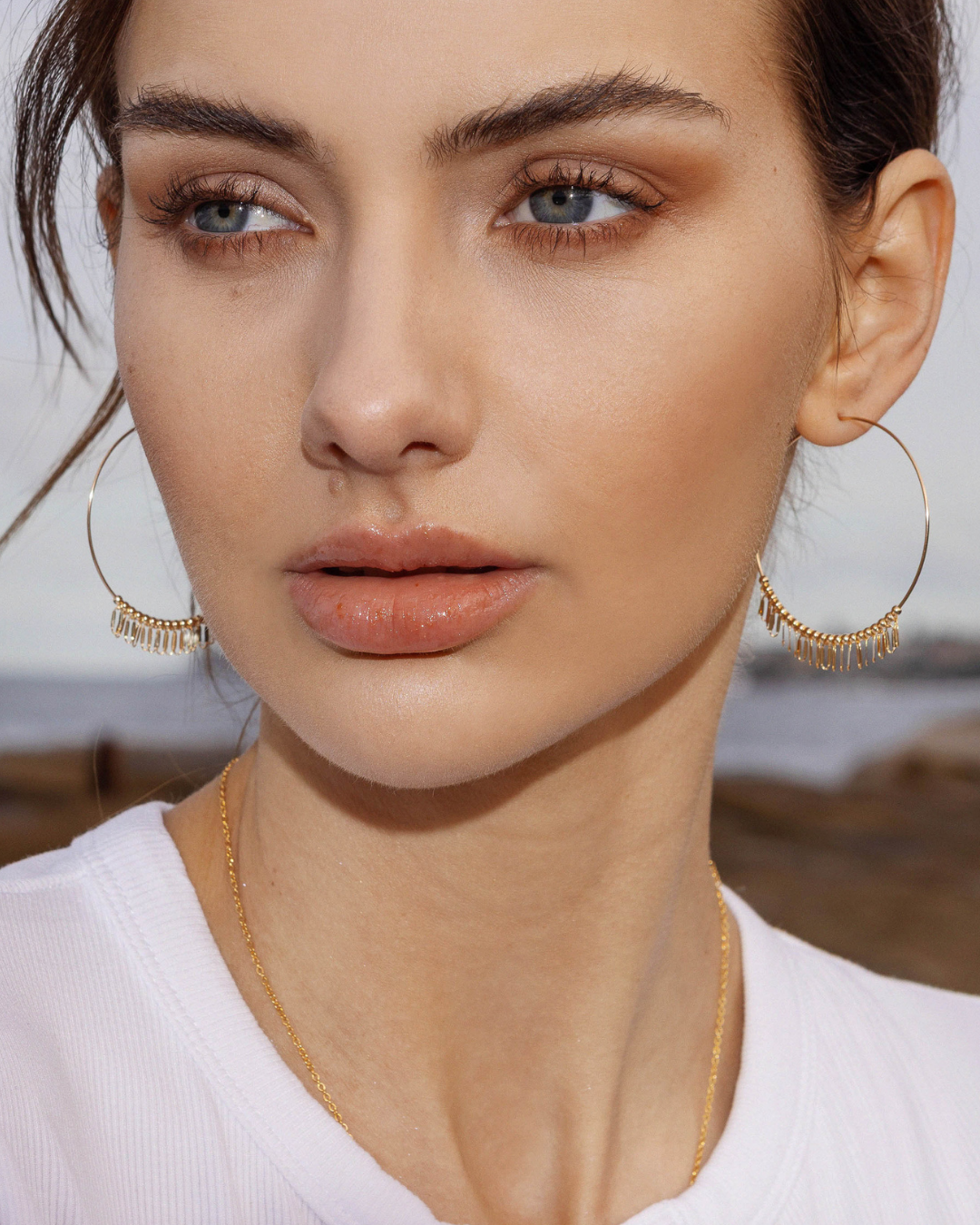 Close-up of a person wearing fine large gold hoop earrings with a blurred background