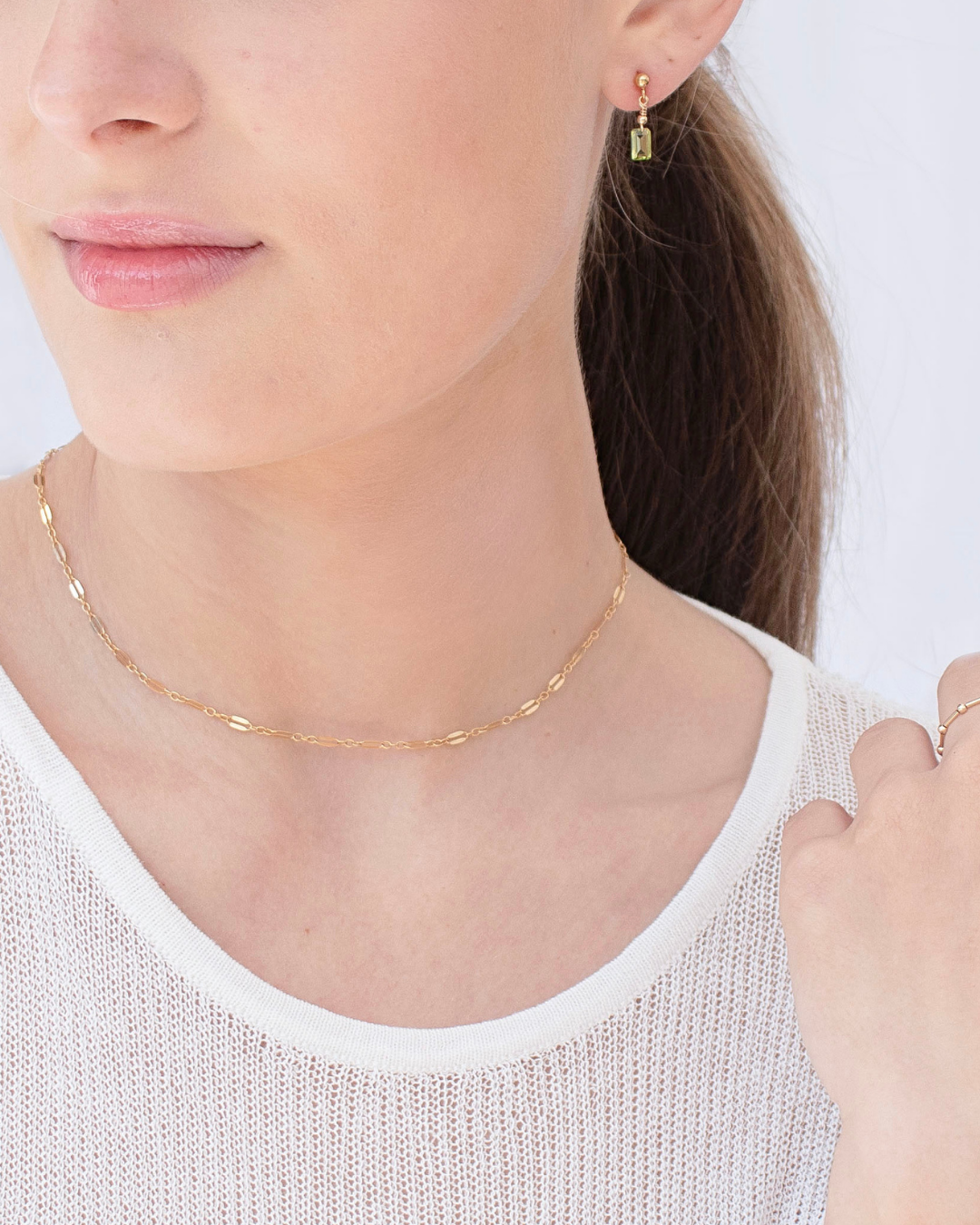 Gold necklace and earring set worn by a person on a light background