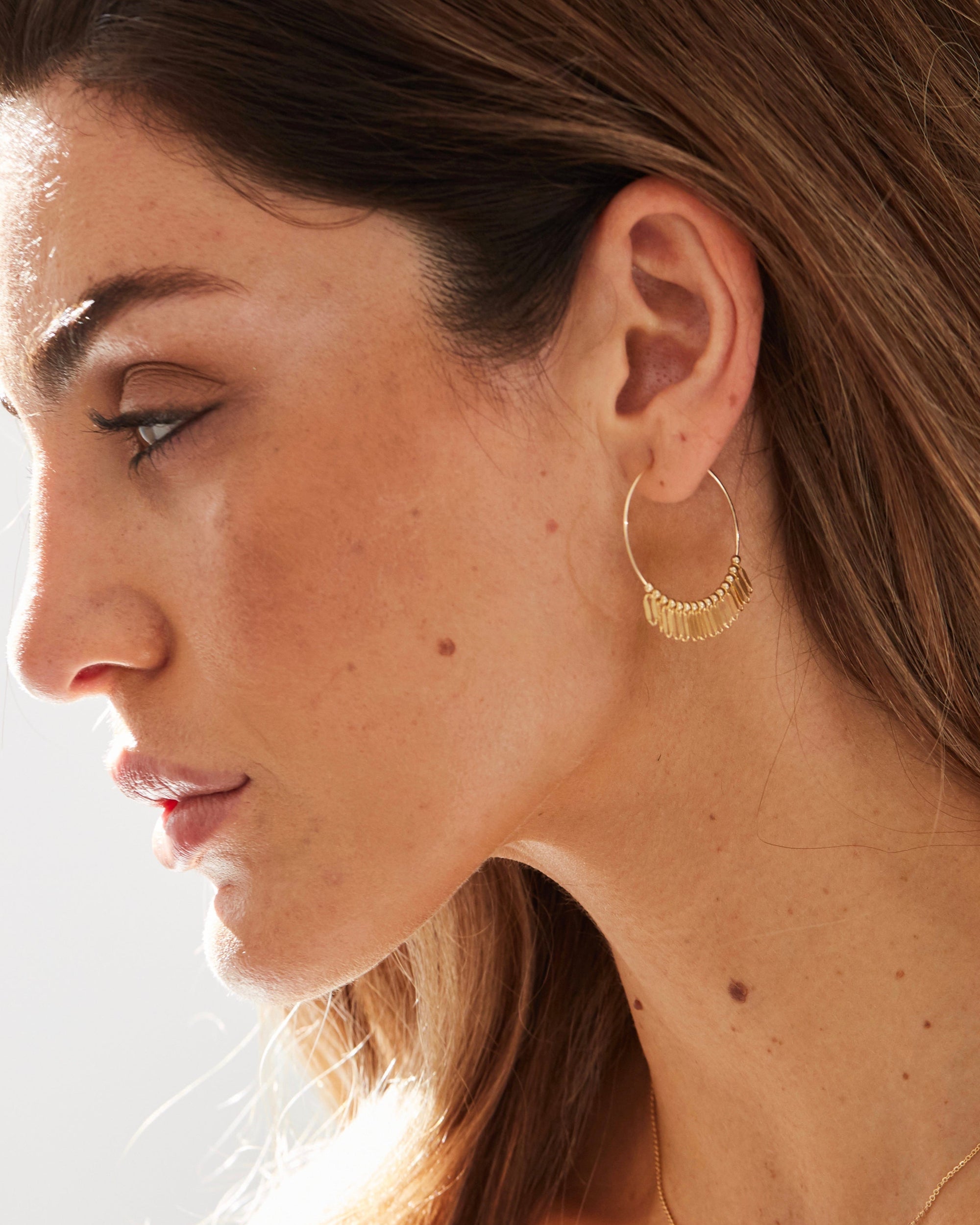 Close-up of a woman wearing a gold hoop earrings with a blurred background