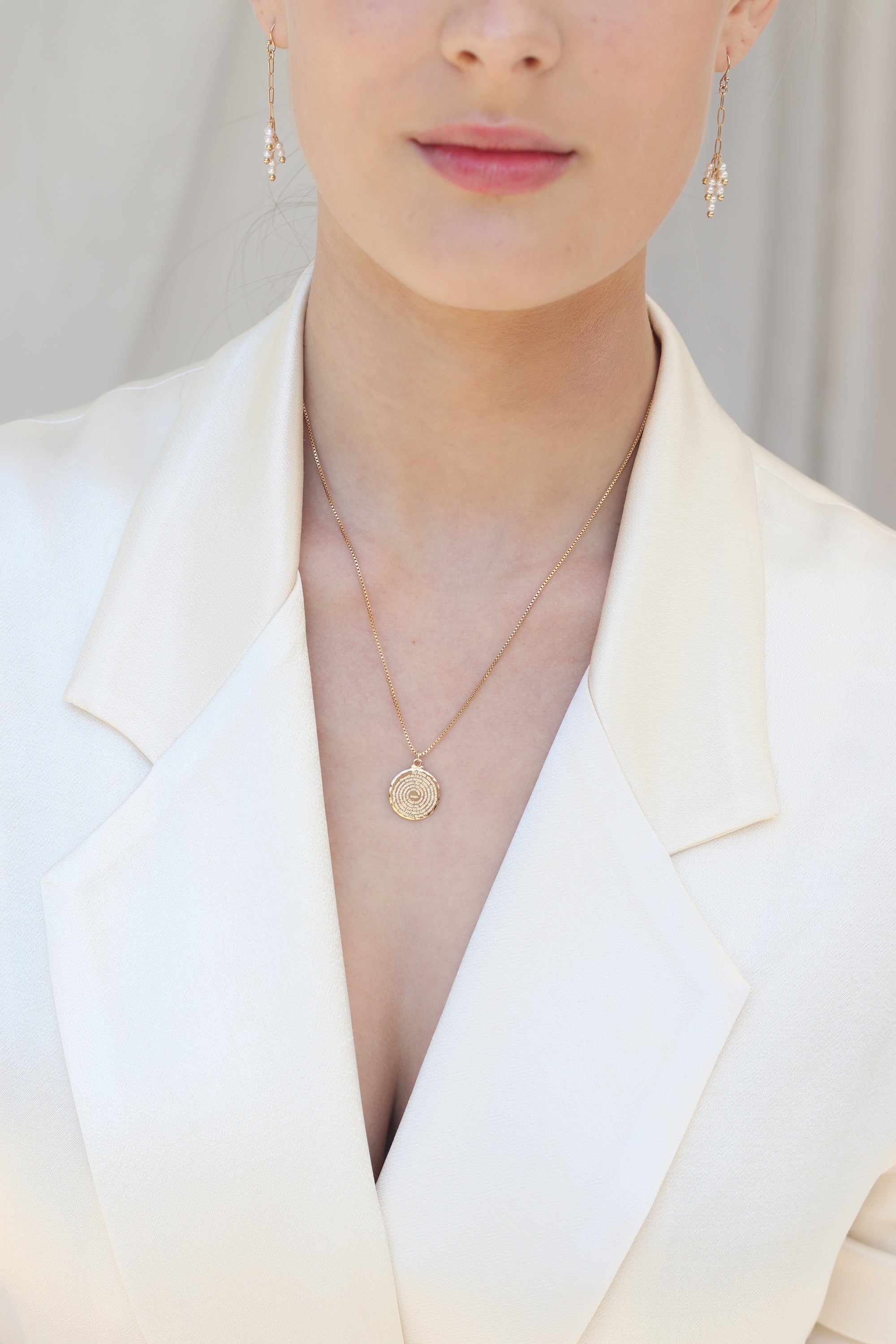 Close-up of a person wearing pearl earrings and a gold pendant necklace.