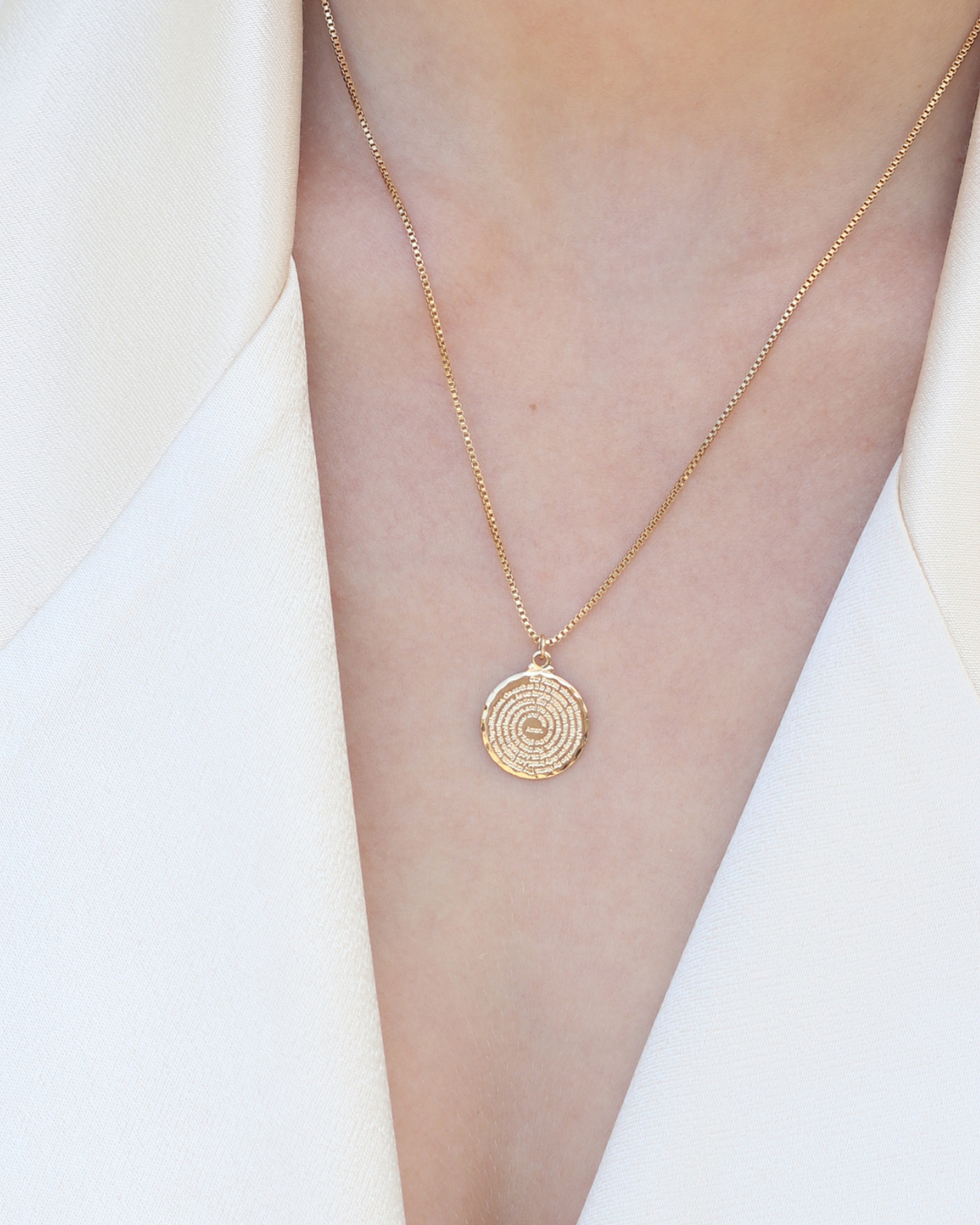 Gold necklace with a circular pendant on a white background