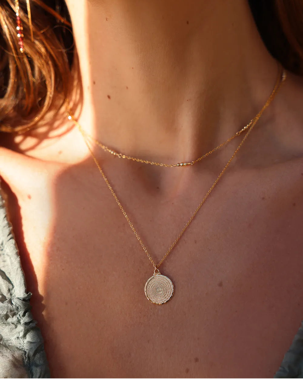 Model wearing gold necklace with a round pendant engraved with 'Our Father ...'