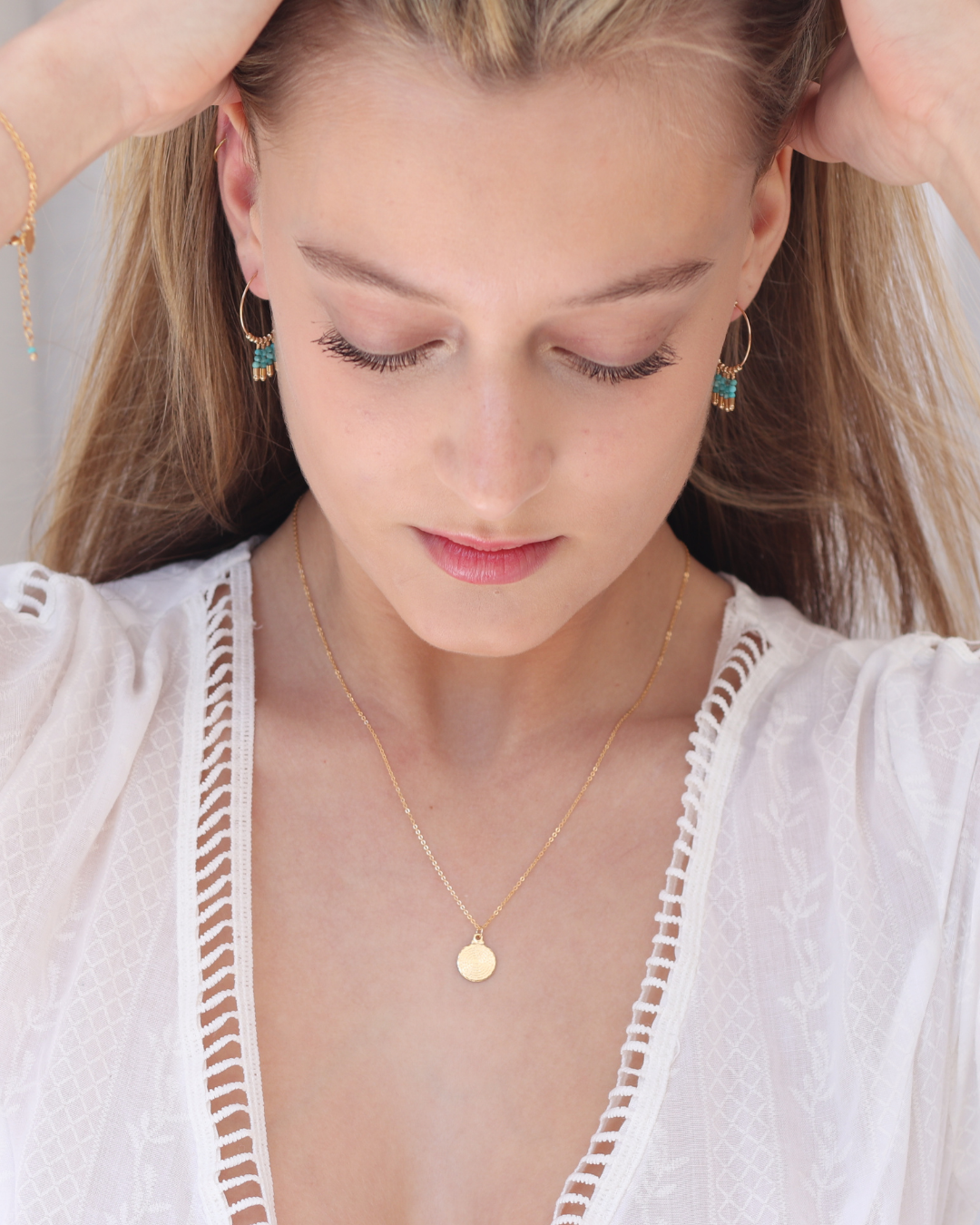 Woman wearing gold necklace and earrings with a white top