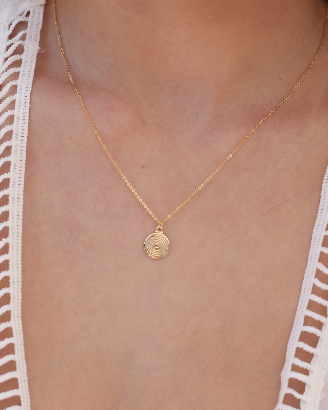 Gold necklace with a pendant on a person wearing a white lace garment.
