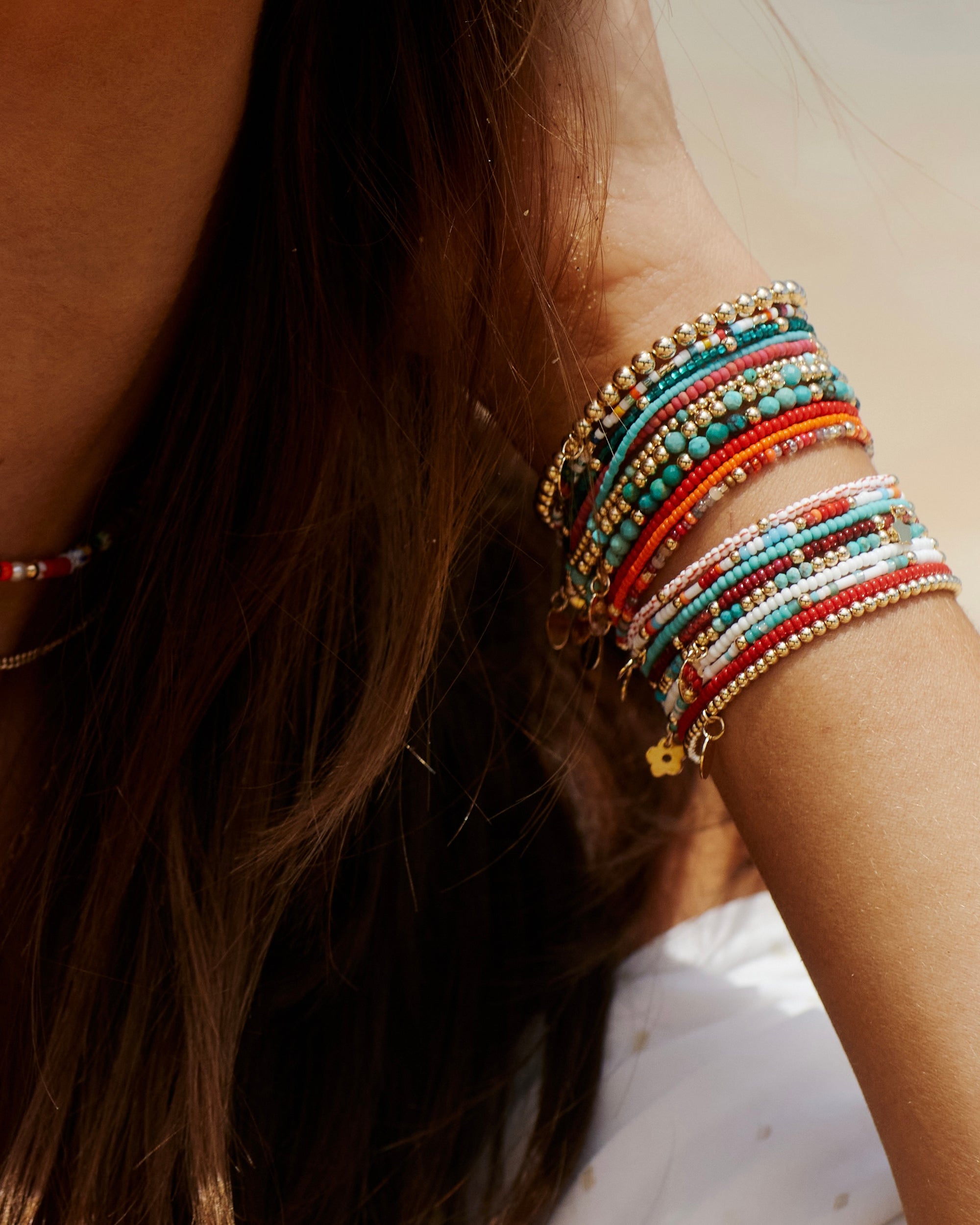 red bead bracelet stacked with multi coloured and gold bracelets