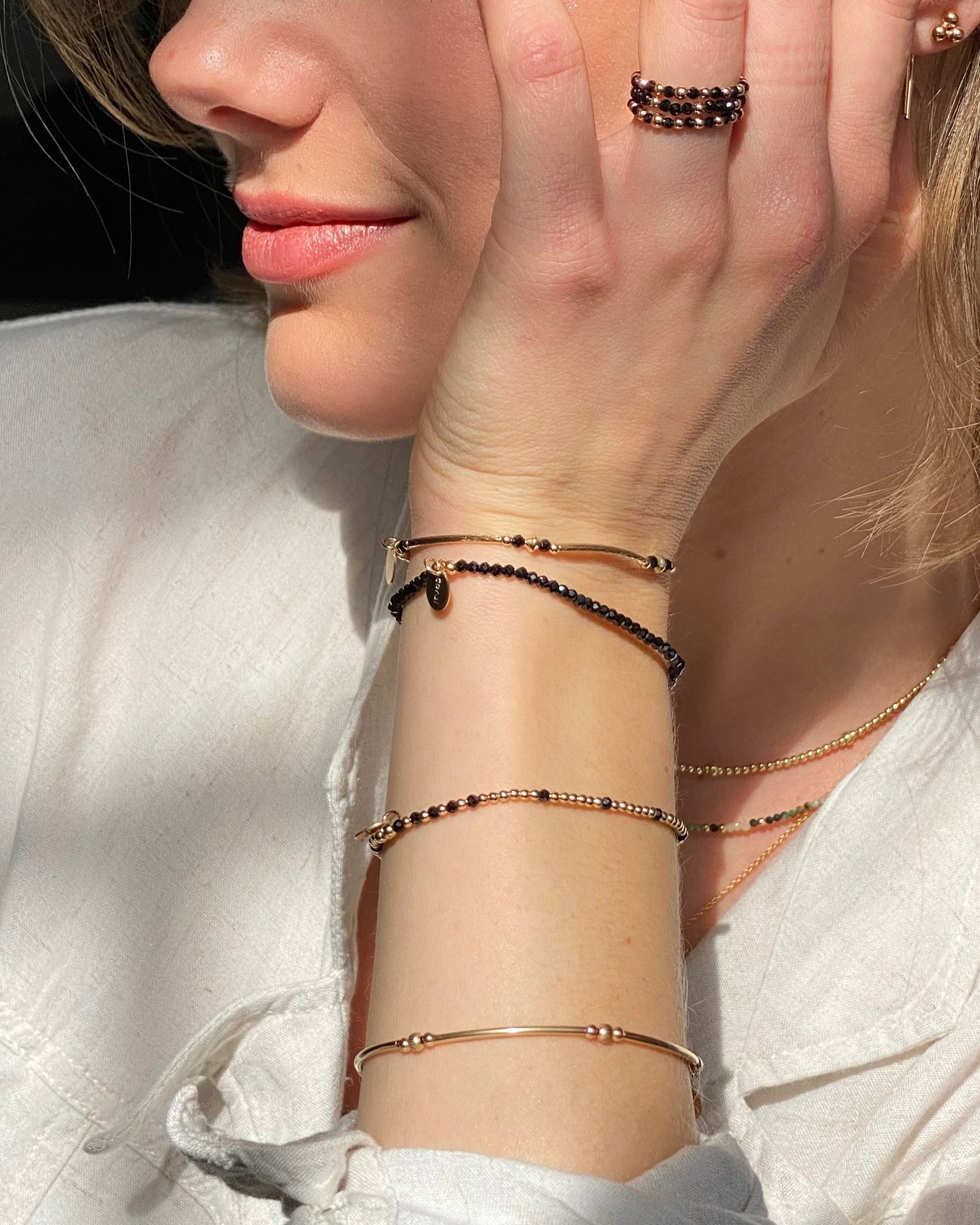 Close-up of a woman wearing multiple bracelets and rings featuring black spinel gemstones on their wrist with a neutral background.