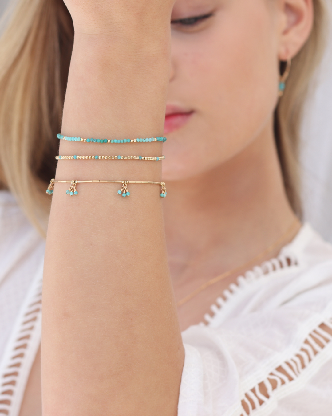Close-up of a person wearing three delicate gold bracelets on a white background