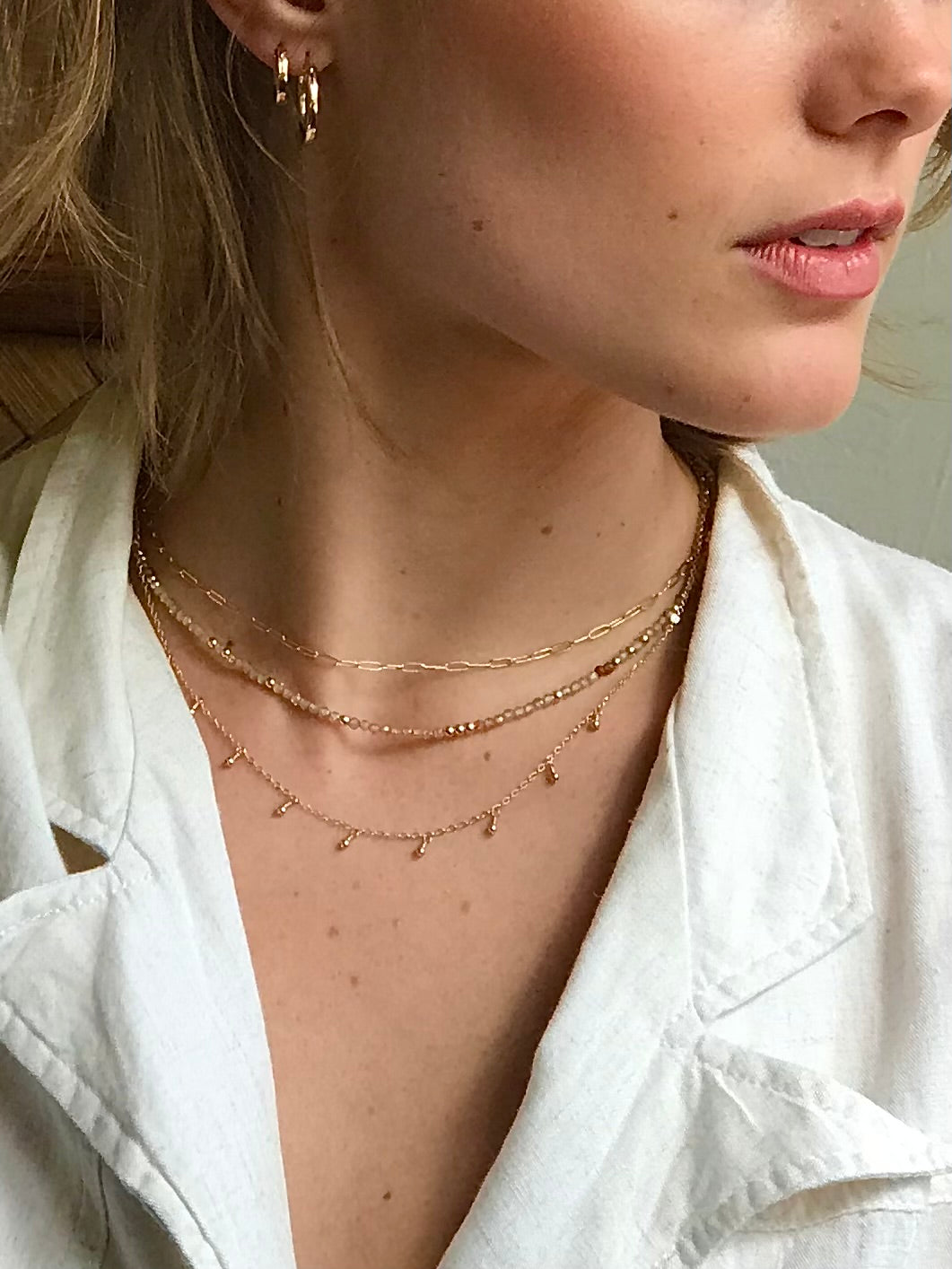 Close-up of a person wearing gold necklaces and earrings with a blurred background