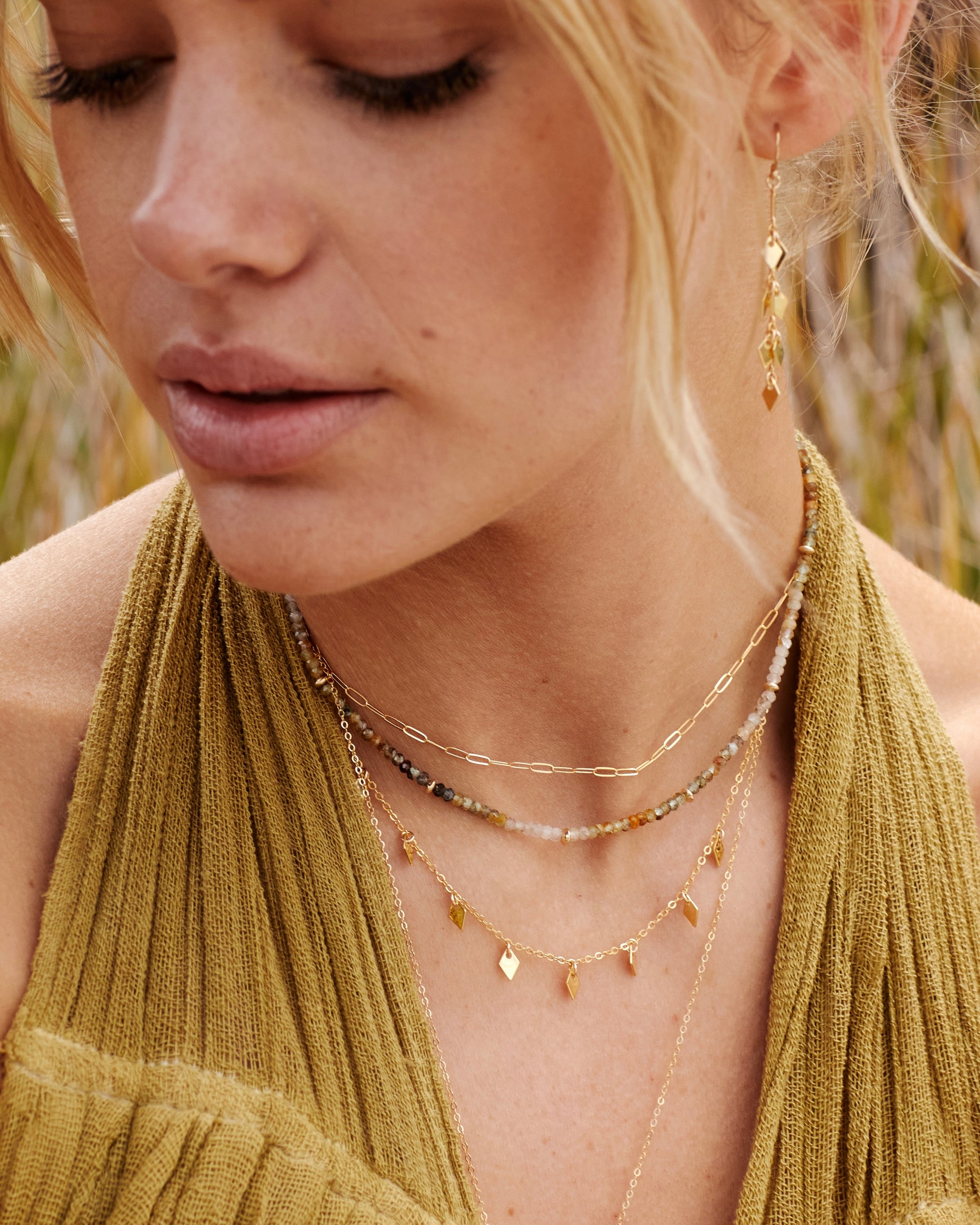 Close-up of a woman wearing layered necklaces and earrings with a blurred natural background