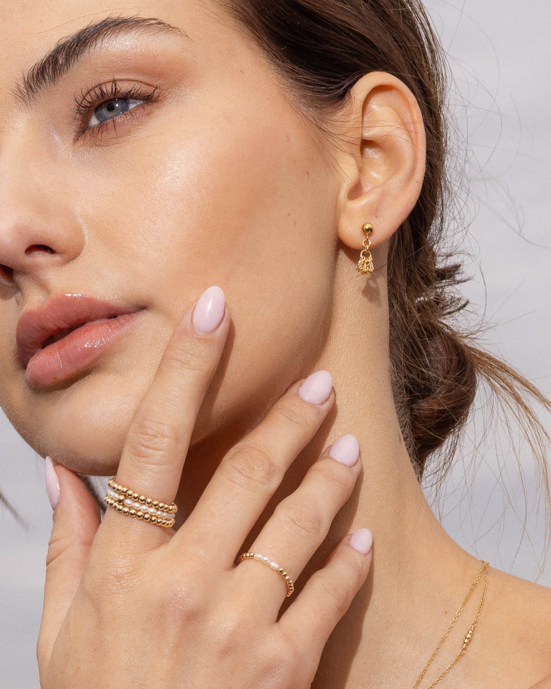 Close-up of a woman wearing gold earrings and rings with a neutral background