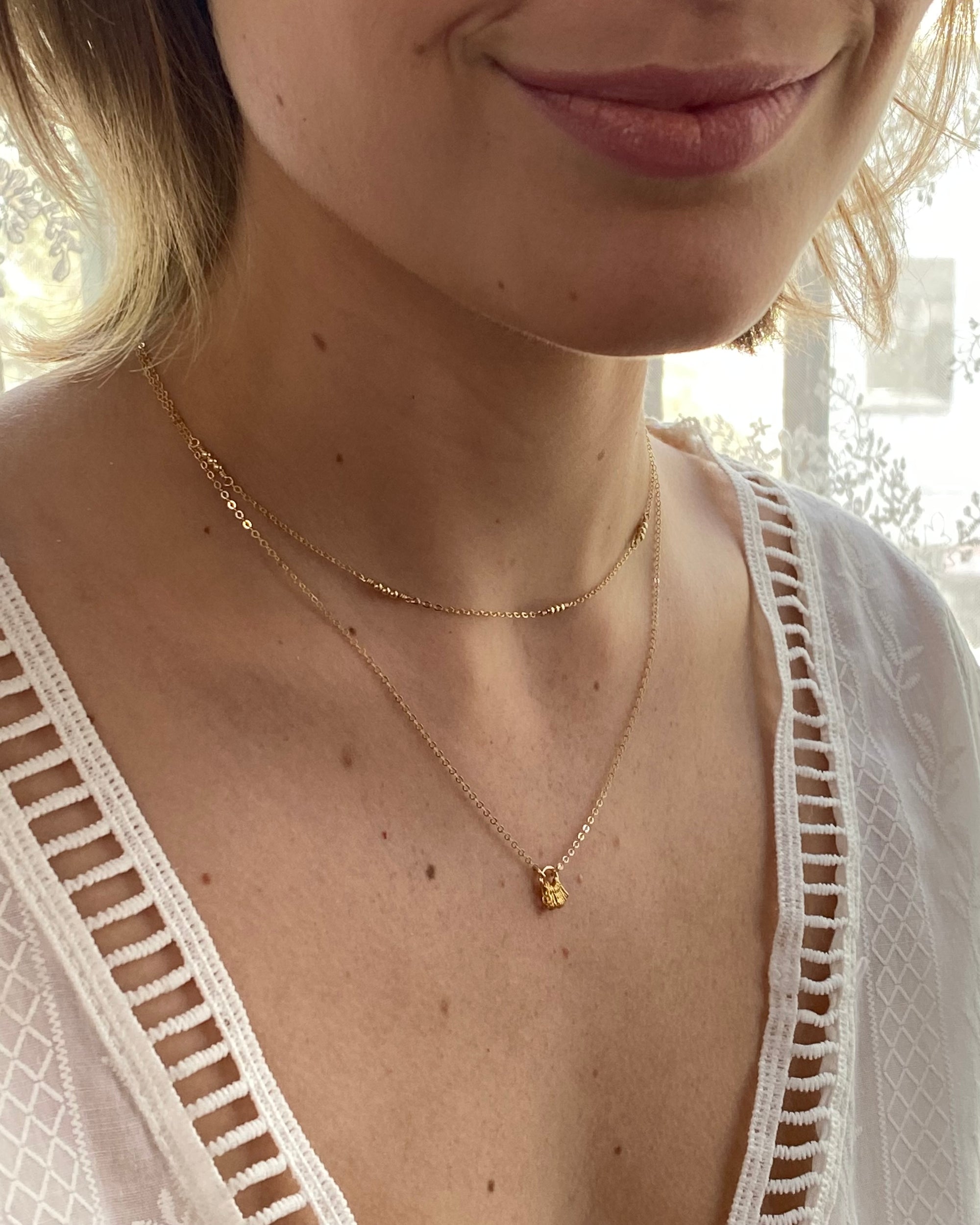 Close-up of a woman wearing a delicate gold necklaces wearing a white lace top