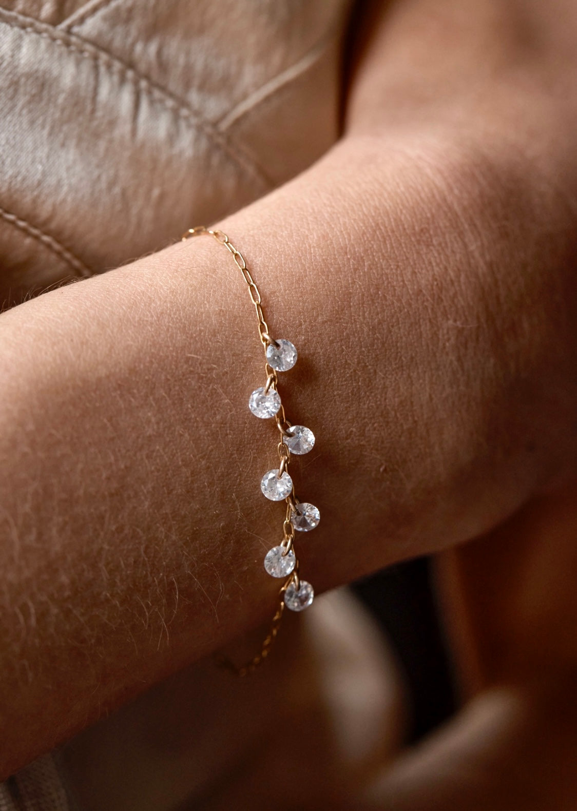 Delicate gold cubic zirconia bracelet on a wrist against a neutral background